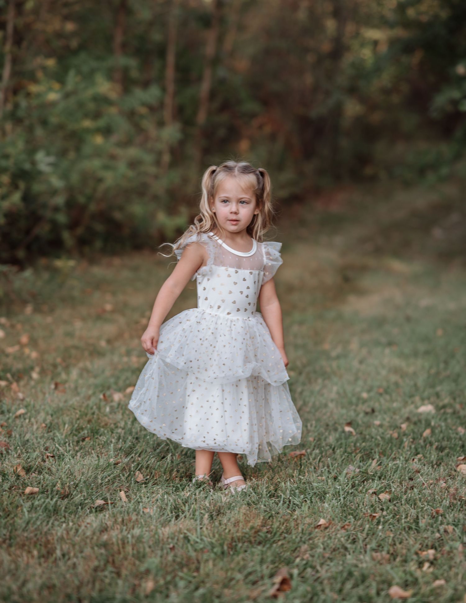 A child in a white polka dot dress twirls and plays on a grassy hill during an outdoor photo session.