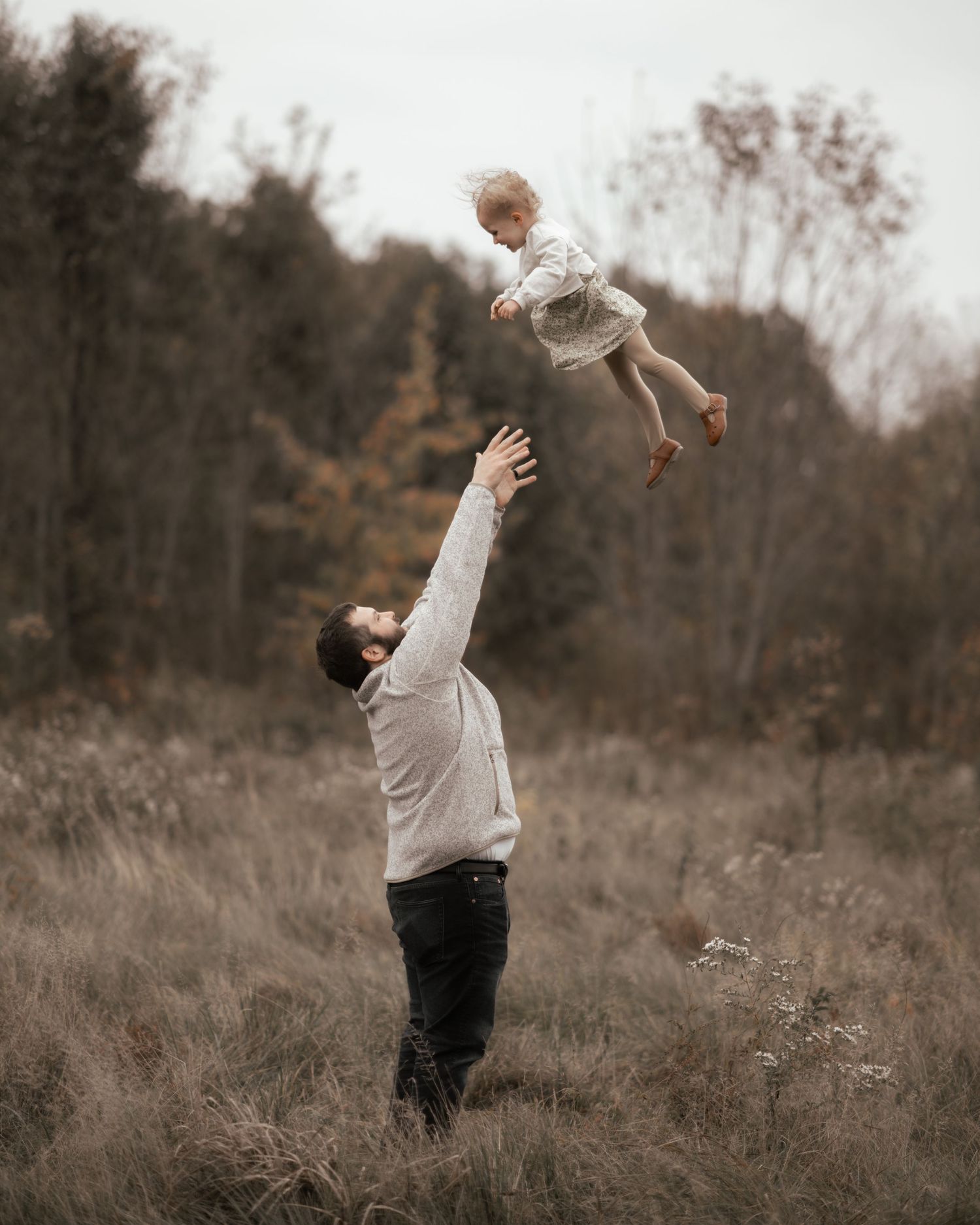 Parent tossing child playfully in air against backdrop of autumn field.