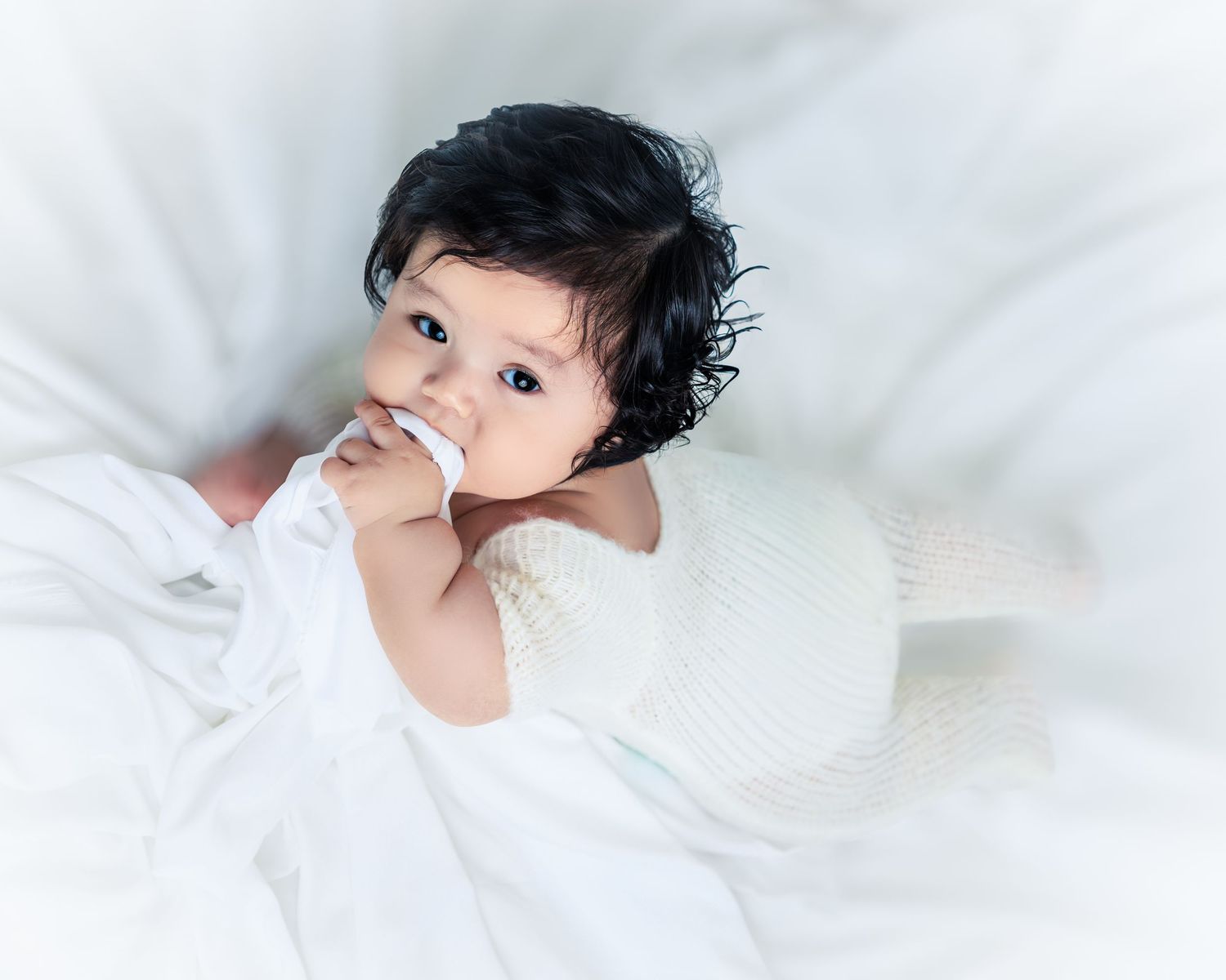 Person with short dark hair lying on white bedding in a dreamy boudoir photography pose.