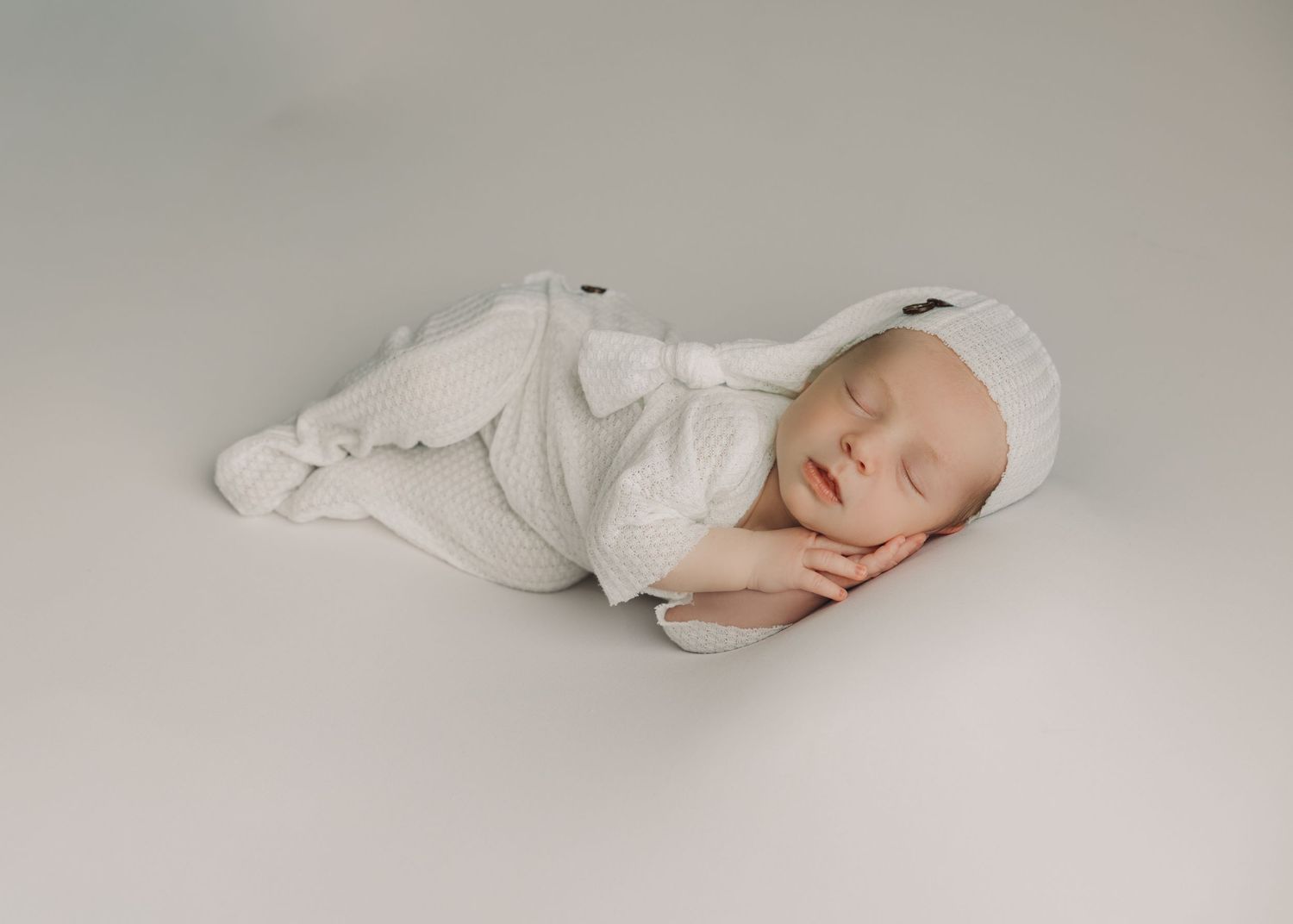 A sleeping baby in white clothing lies peacefully on a light gray background in a series of connected photos.