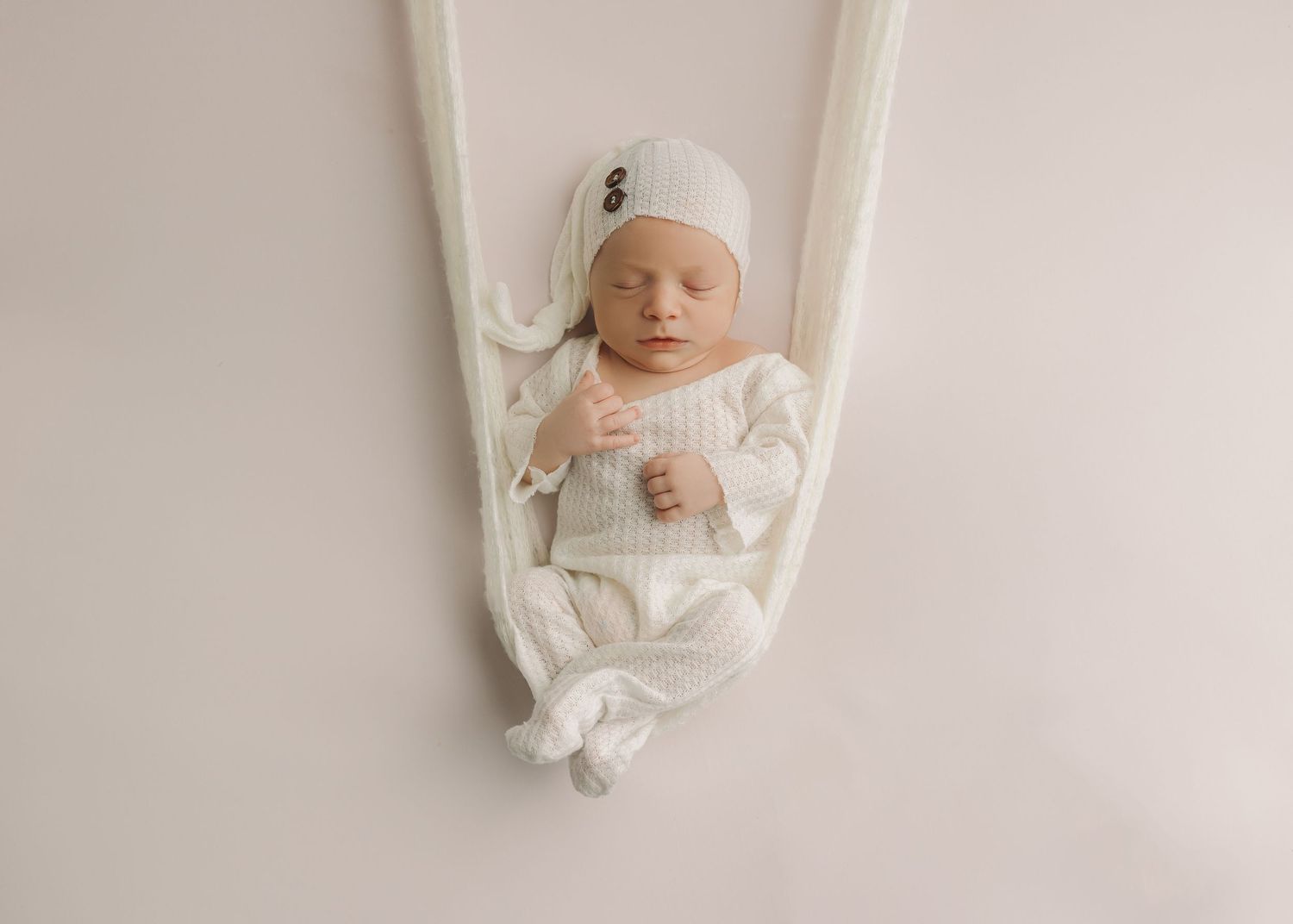 Minimalist white newborn photography session with baby wrapped in soft fabric on neutral backdrop.