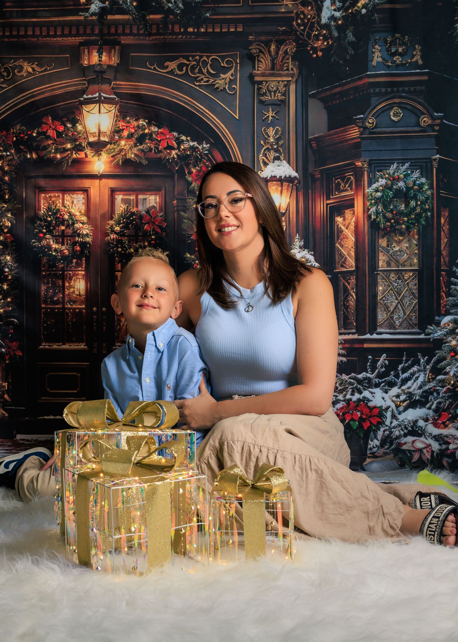A woman and young boy pose together in front of a festive Christmas backdrop with golden gift boxes.