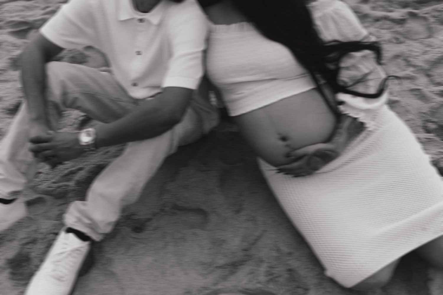 Black and white intimate maternity photo of couple relaxing on sand.