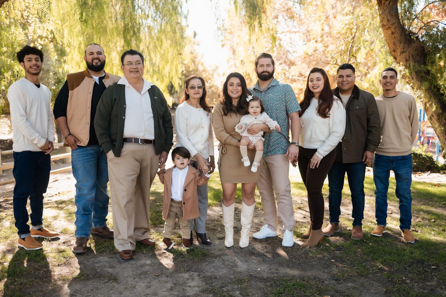 Extended family group poses together under willow tree for outdoor portrait session.