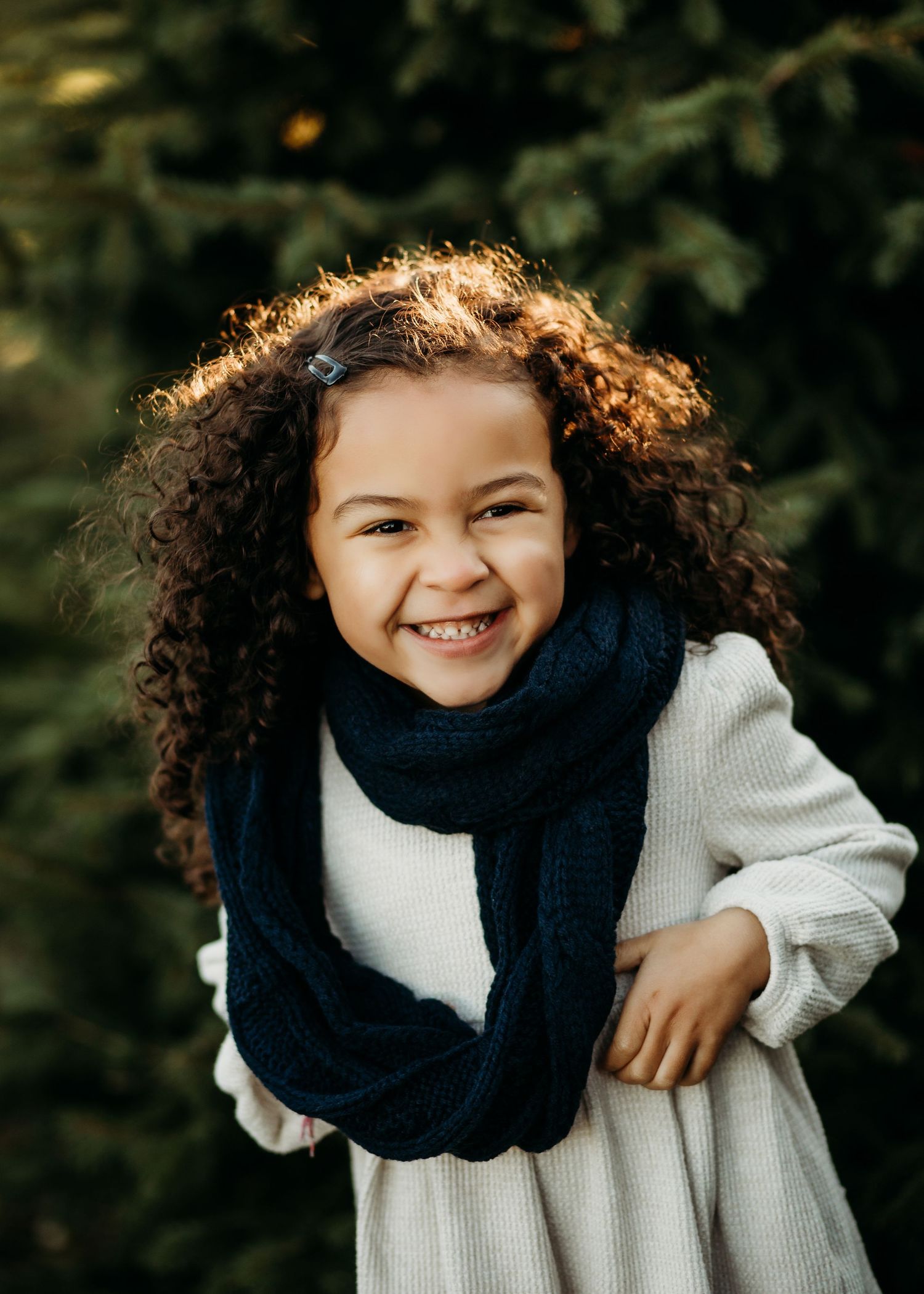 A child in a navy blue scarf and white sweater smiles warmly while playing outdoors in autumn.