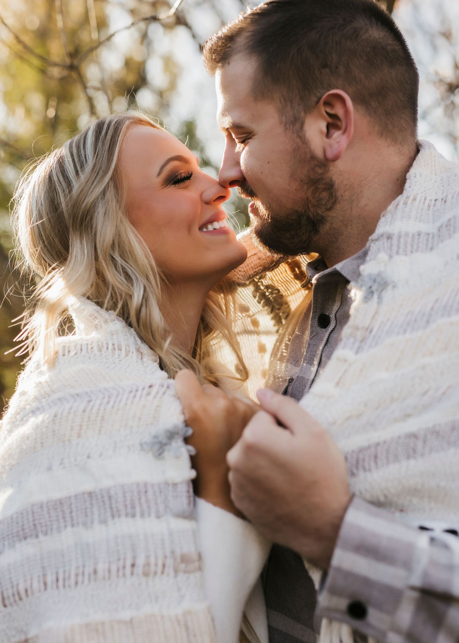 Romantic couple wrapped in a striped blanket share an intimate moment in warm autumn sunlight.