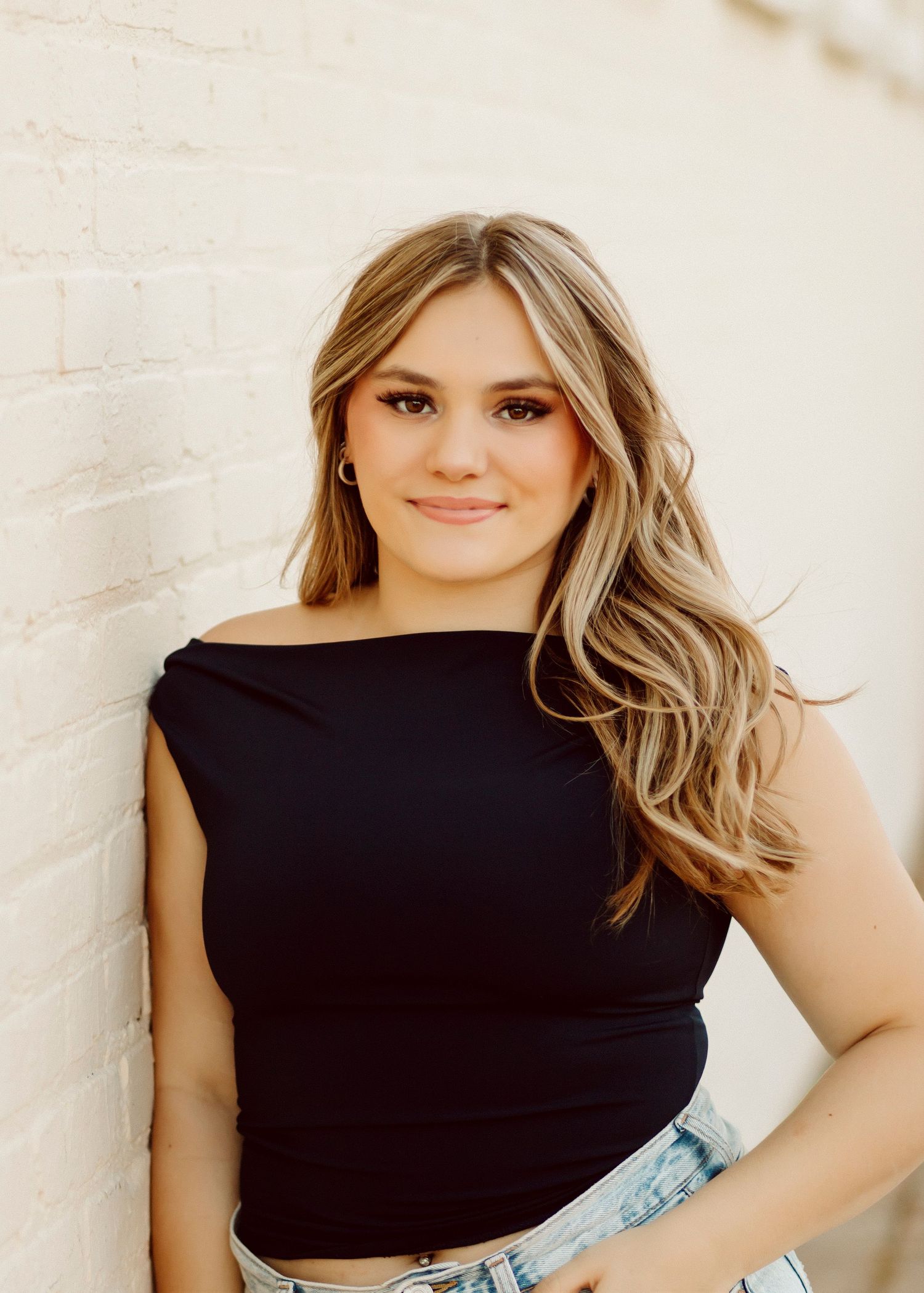 Woman in black sleeveless top poses against white brick wall.