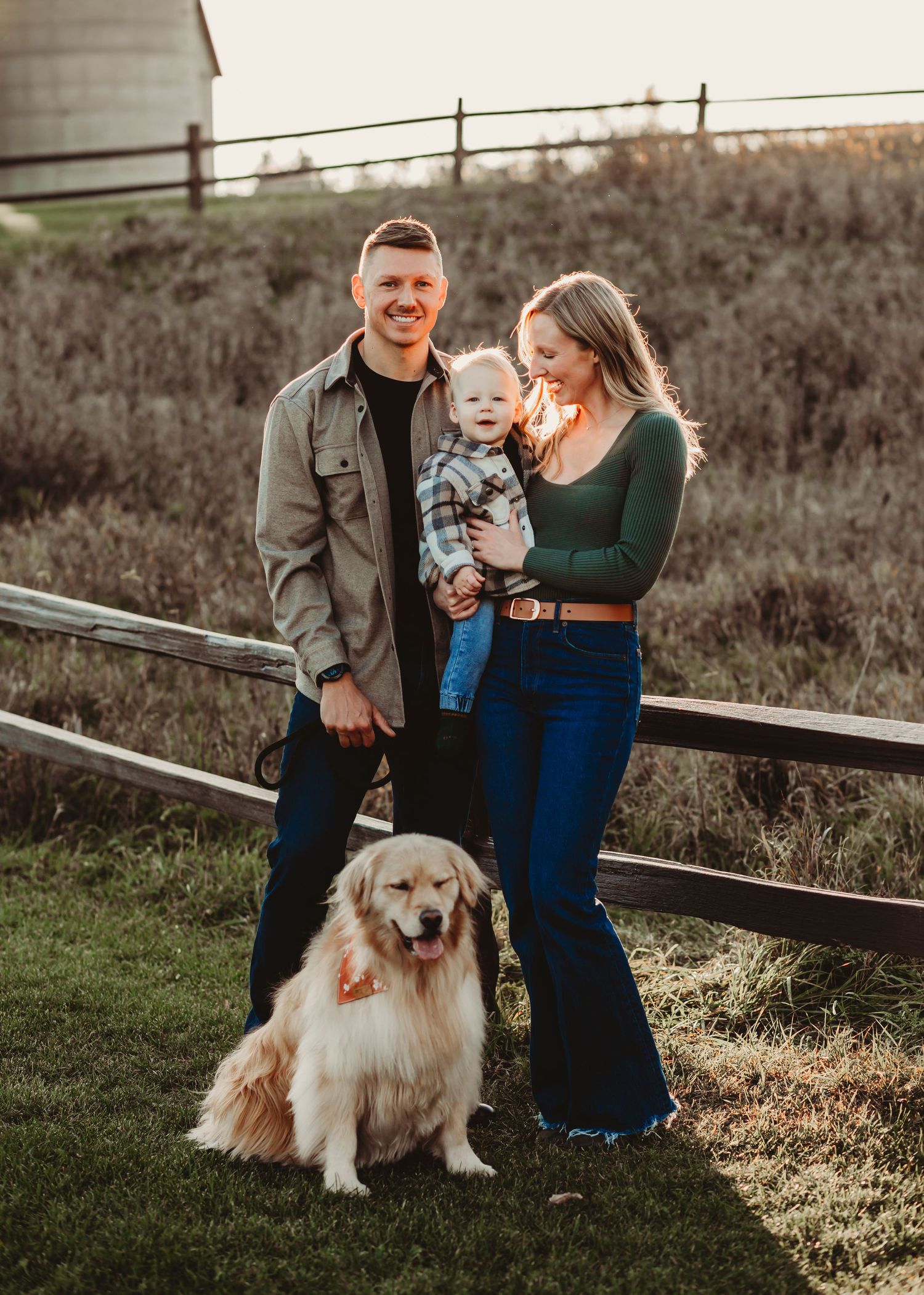 Family and golden retriever dog pose together on grassy hillside during sunset photo session.