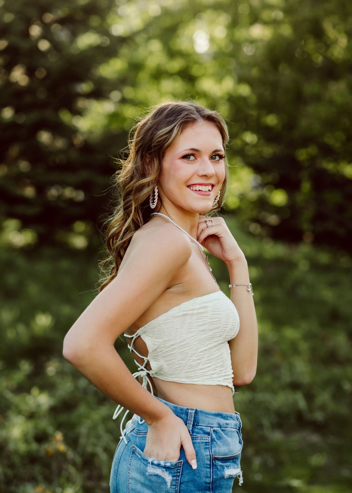 Woman in white crop top and jeans poses outdoors in natural lighting.