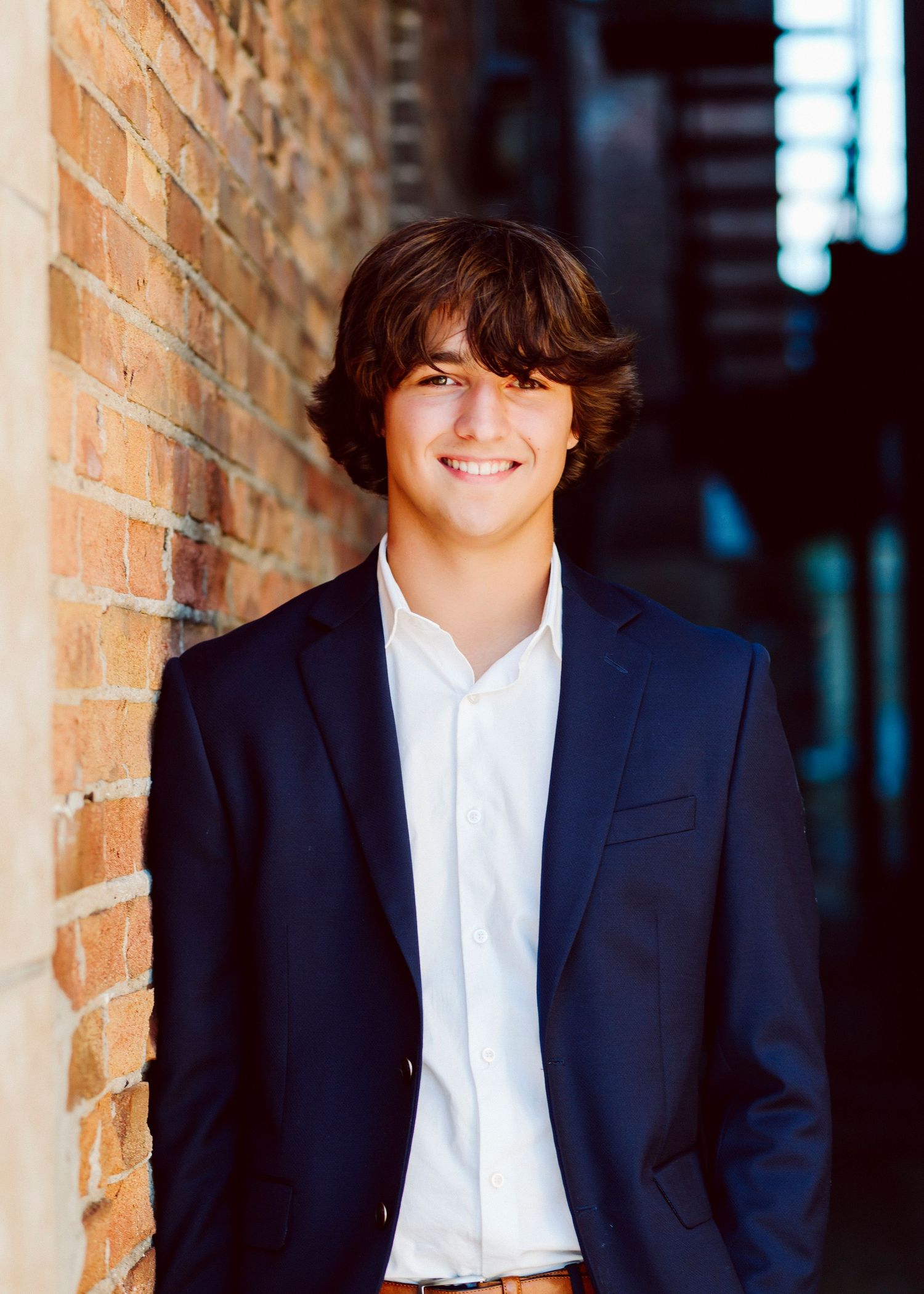 Professional headshots against brick wall wearing navy suit and white shirt.