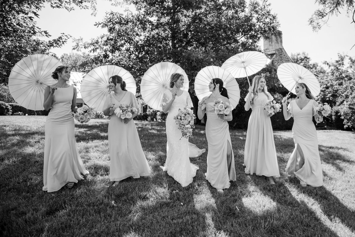 A group in light dresses holding white parasols outdoors on a sunny day.