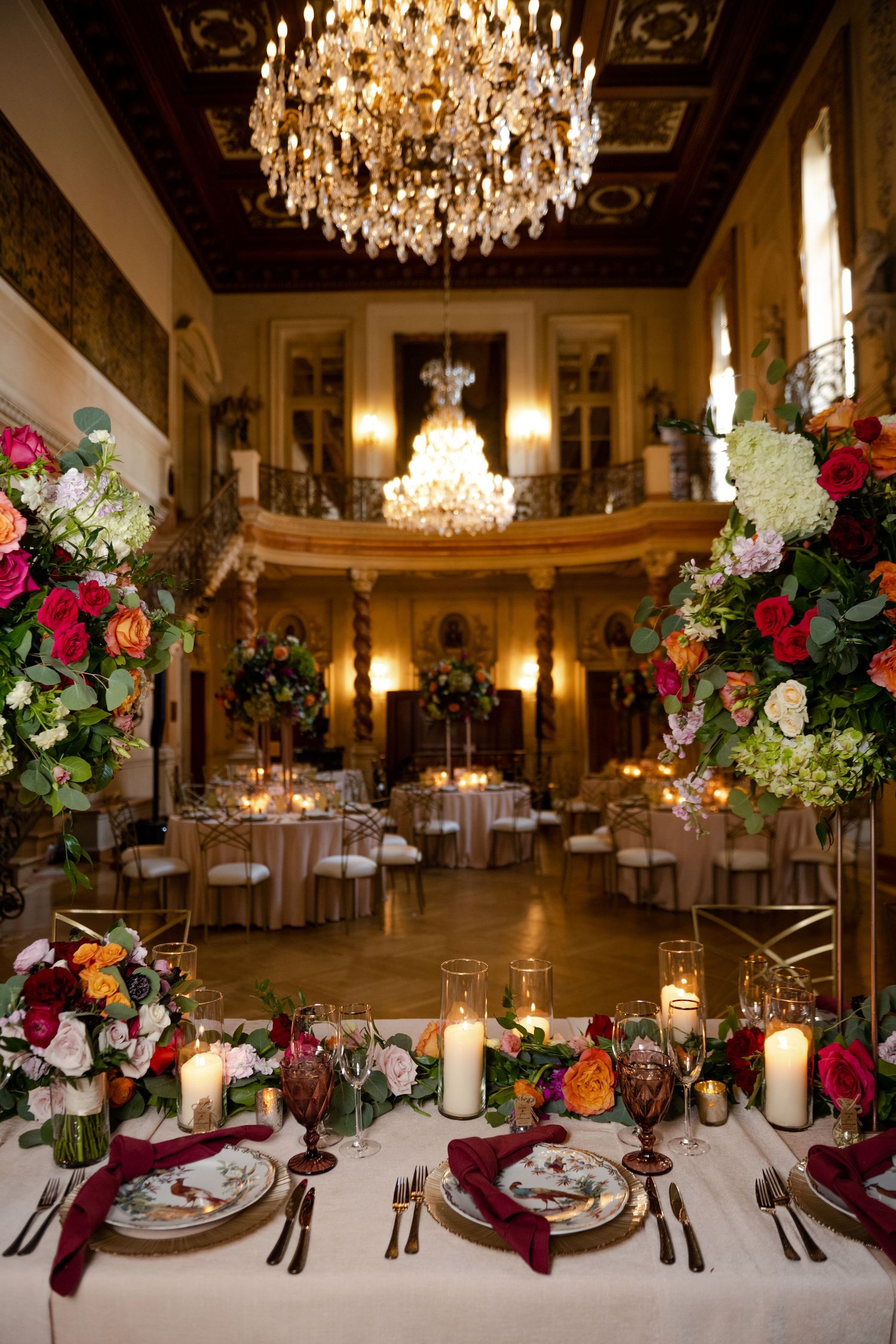 Opulent ballroom with crystal chandeliers and floral arrangements set for elegant wedding reception.