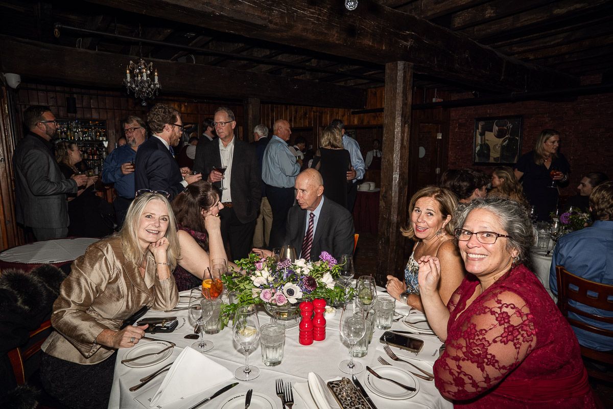 People gathered at tables during an evening event with dim lighting and table settings.