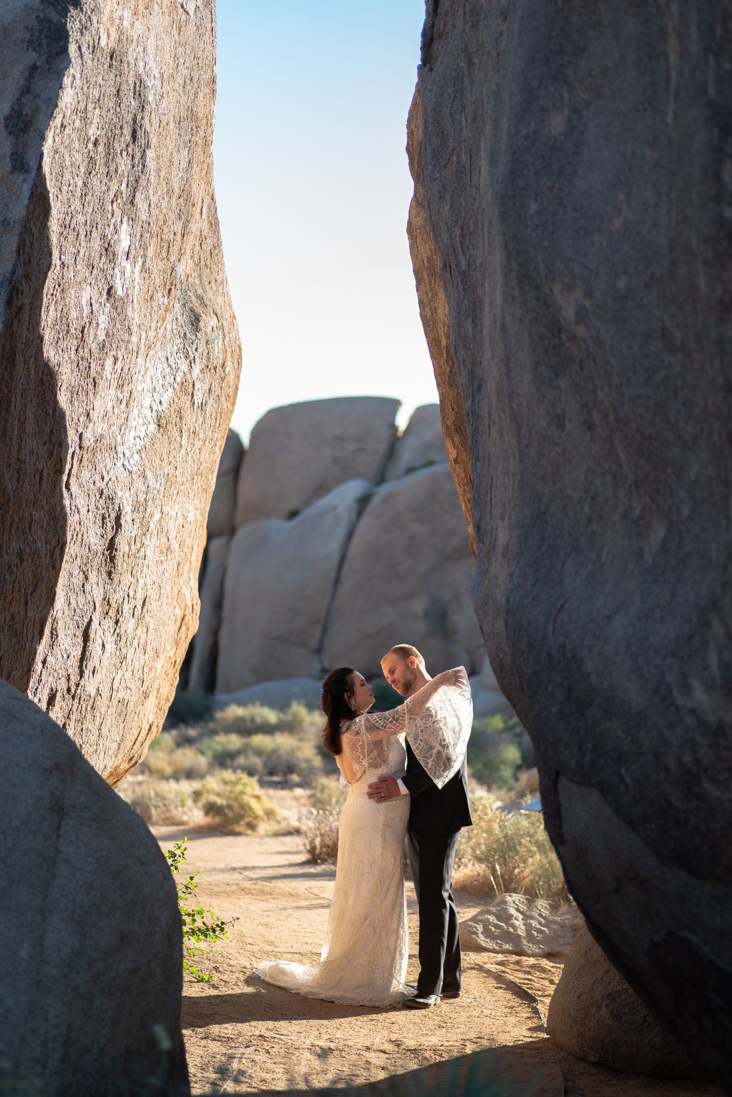 A couple embraces in an intimate moment framed by towering desert rock formations at Joshua Tree National Park.