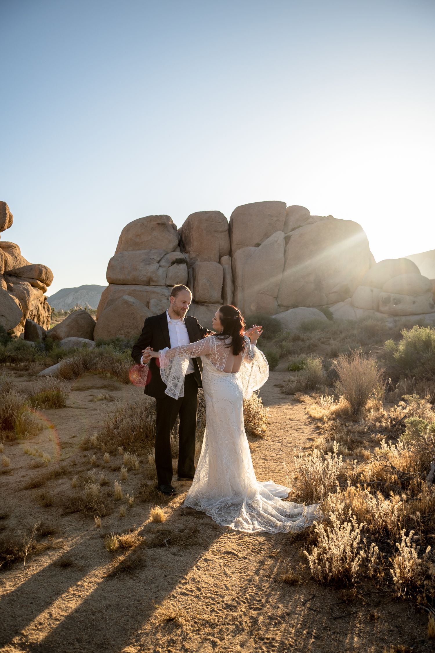 A couple shares a tender moment among large desert boulders at sunrise.