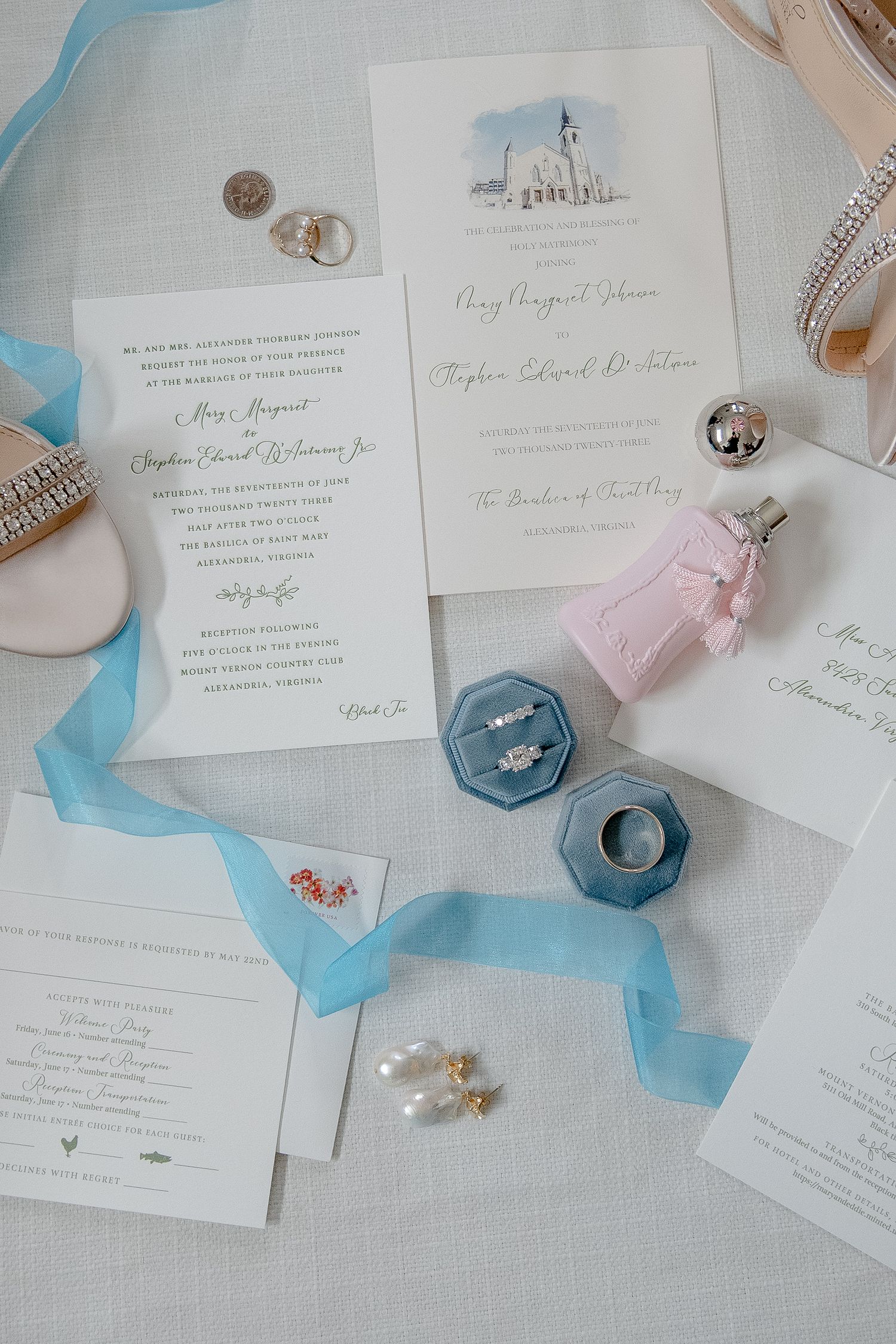 Wedding invitation suite with blue ribbon, wedding rings in velvet boxes and delicate watercolor design on white paper.