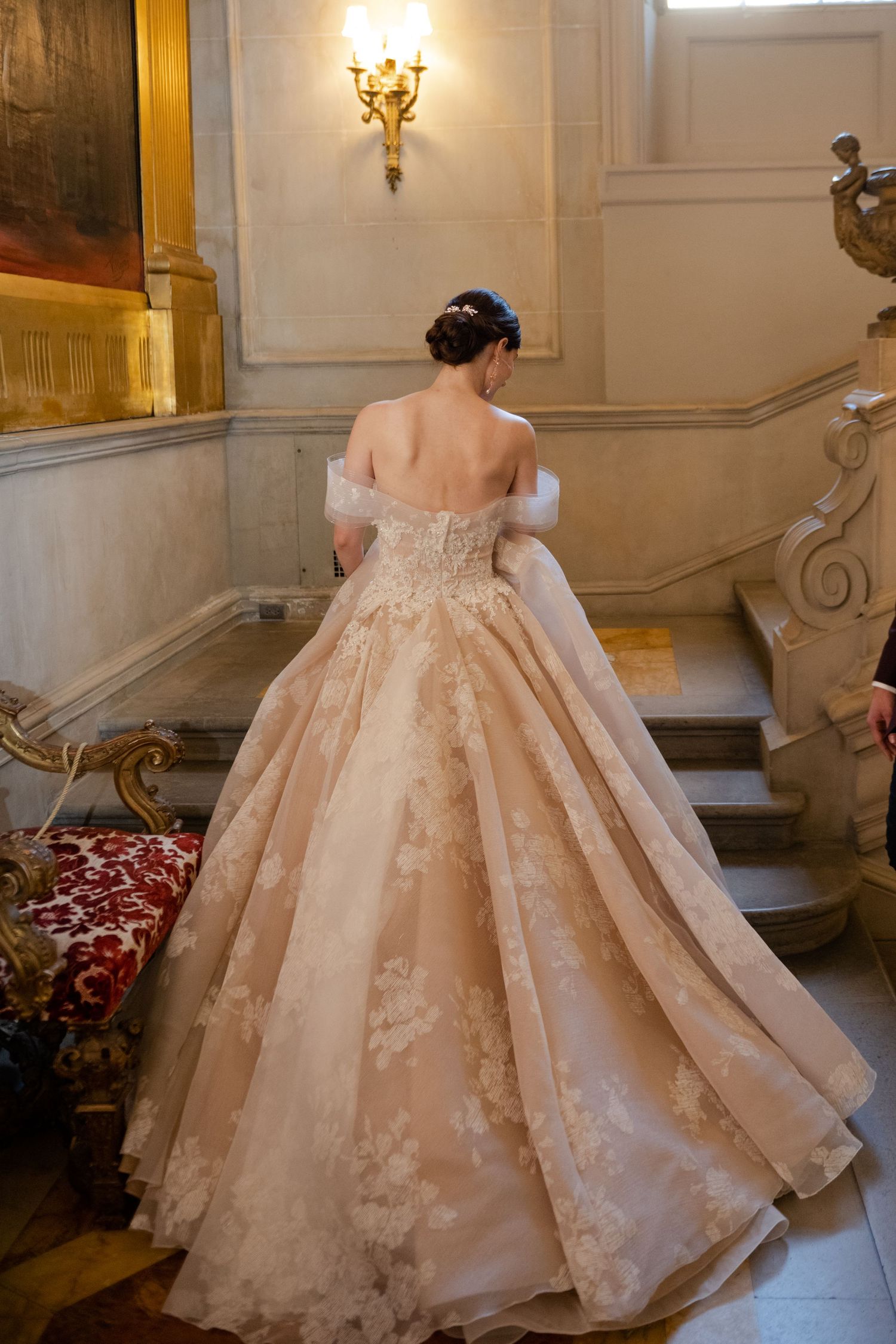 Stunning off-shoulder champagne ballgown with intricate lace details photographed on grand staircase.