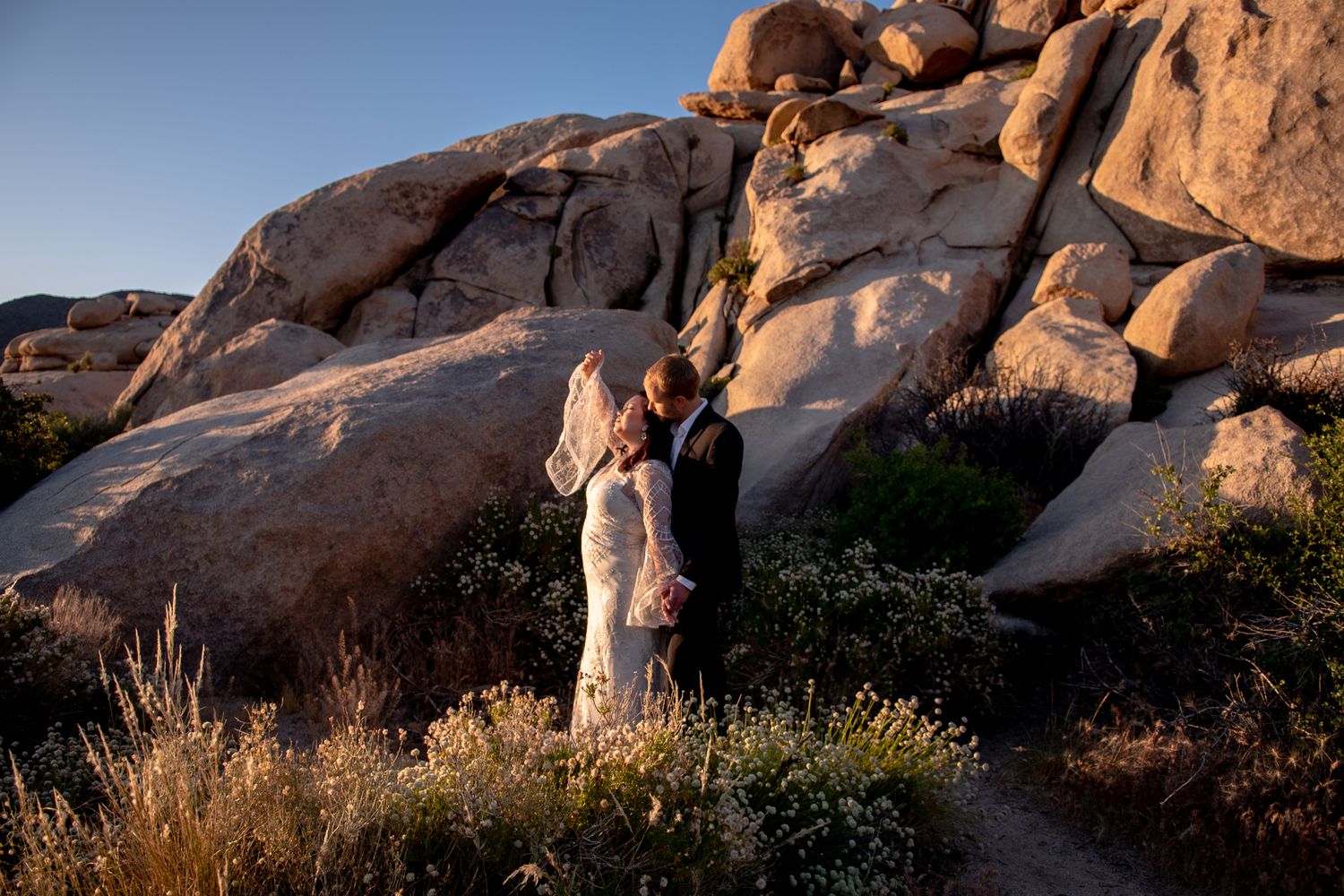 A wedding portrait against massive desert boulders at sunrise.