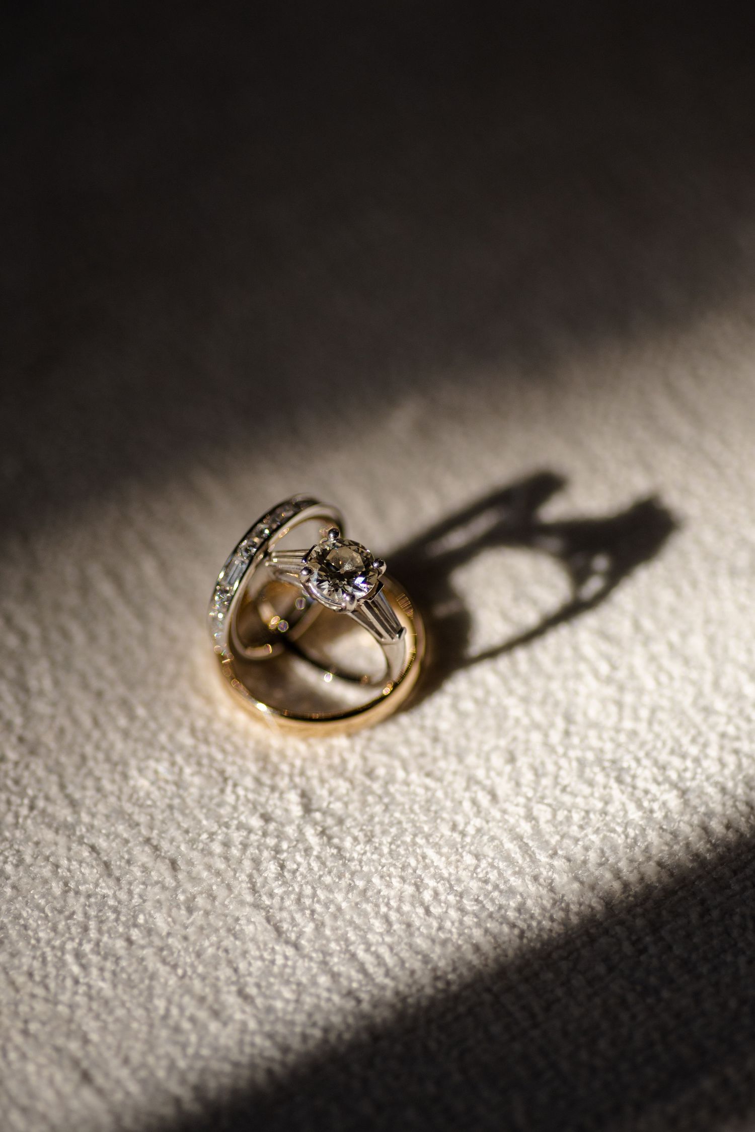 Gold engagement ring with diamond casting dramatic shadow on textured white surface.