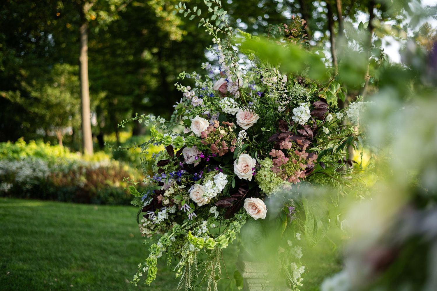 Lush floral arrangement with pink roses and greenery displayed in outdoor garden setting.