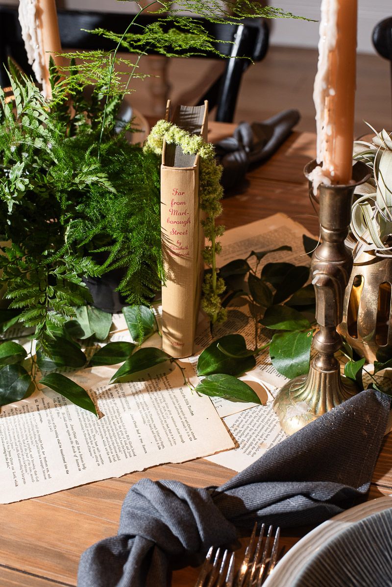 Rustic table setting with wooden candlesticks, greenery, and printed menus on a dark wooden surface.