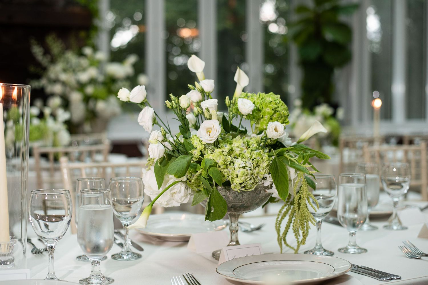 Elegant wedding reception table setting with white floral centerpiece and crystal glassware on white tablecloth.