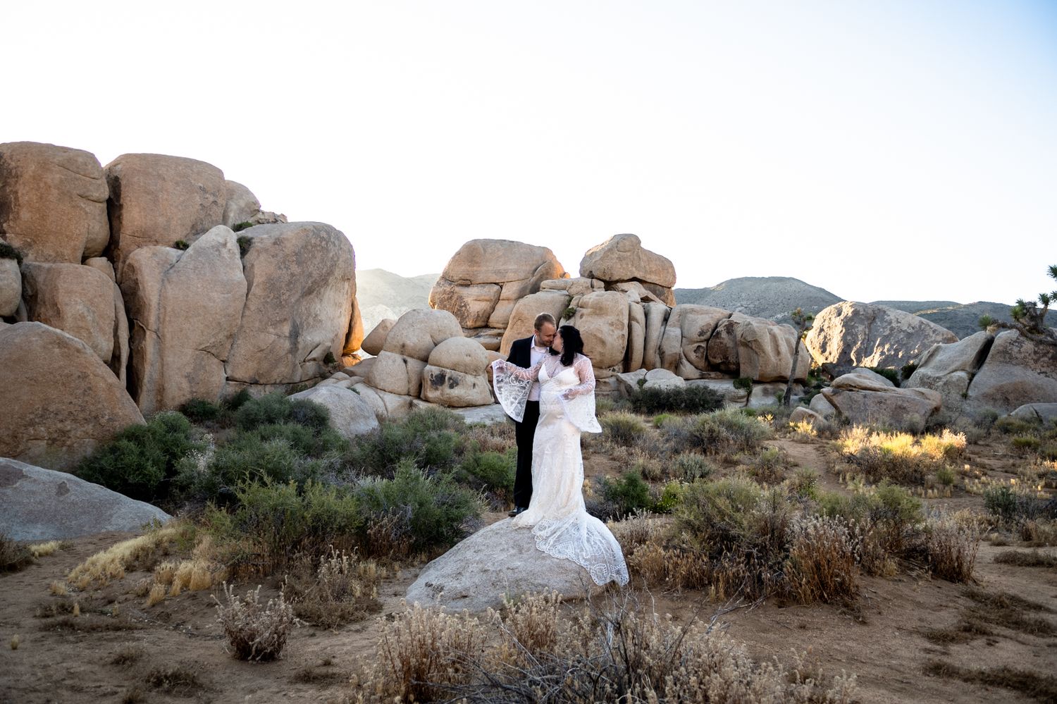 Wedding couple standing on rocks in Joshua Tree National Park during sunset.