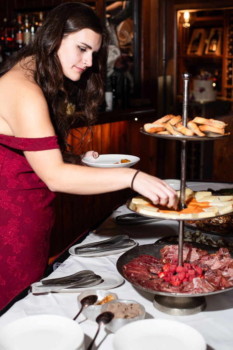 A person in a burgundy dress serves food from elegant platters at a formal dining event.