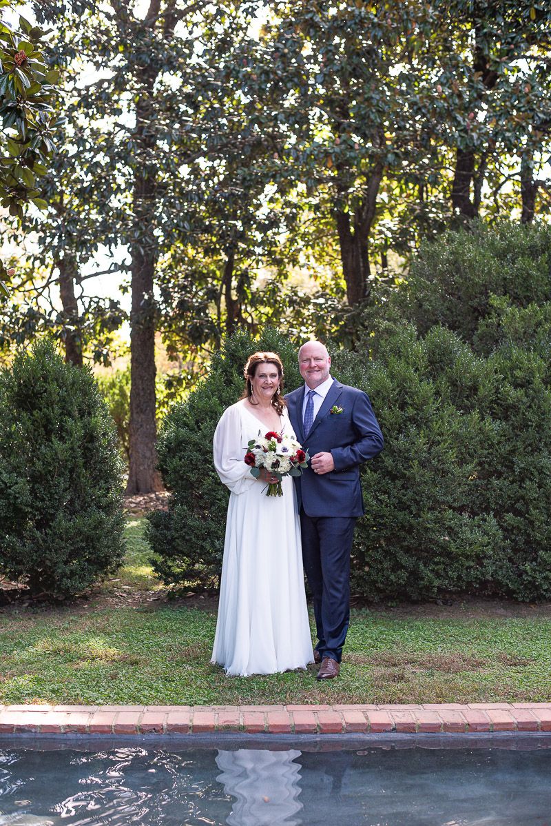 A couple poses for wedding photos in a garden setting with trees and greenery in the background.