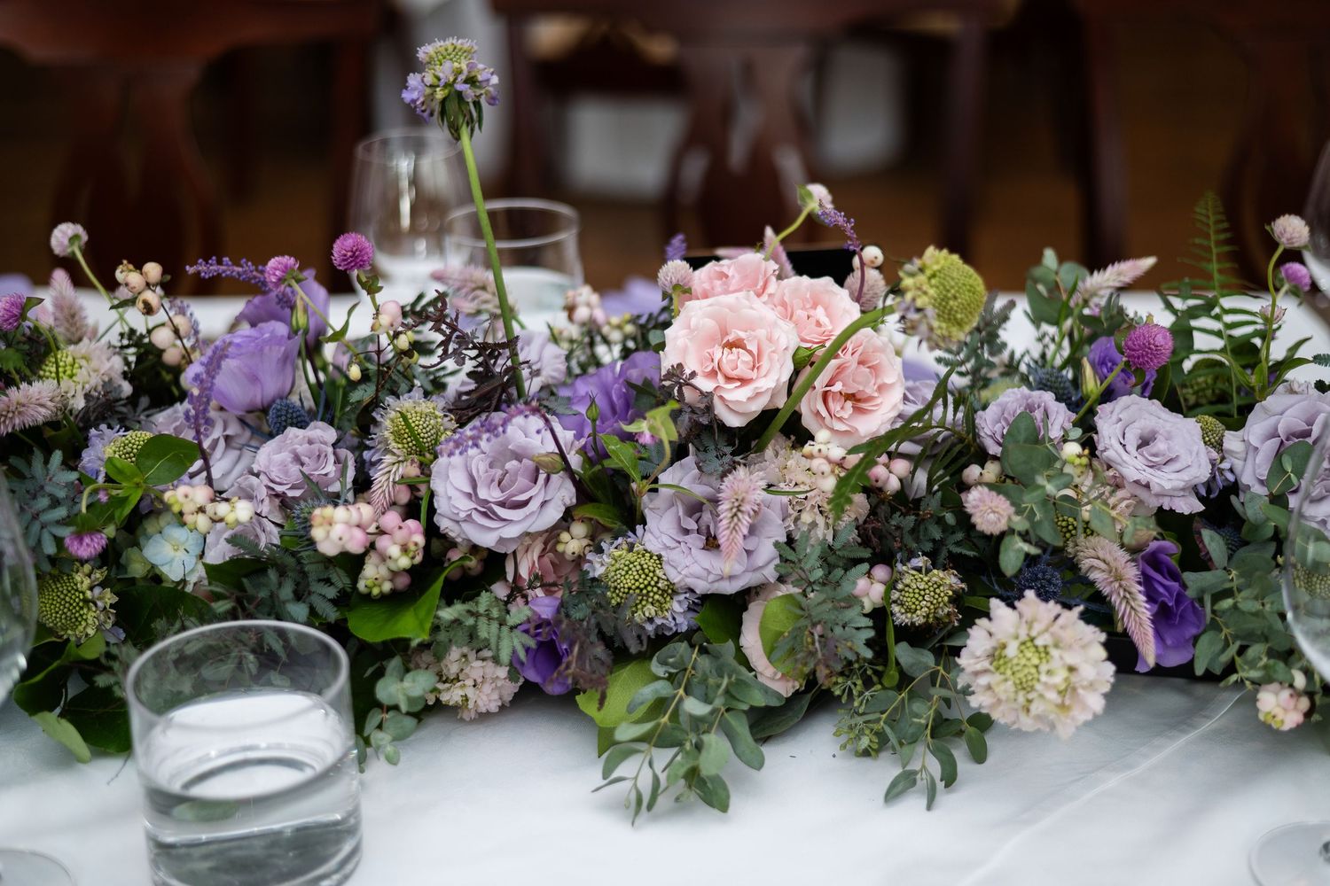 Elegant floral centerpiece with purple and pink roses mixed with greenery.