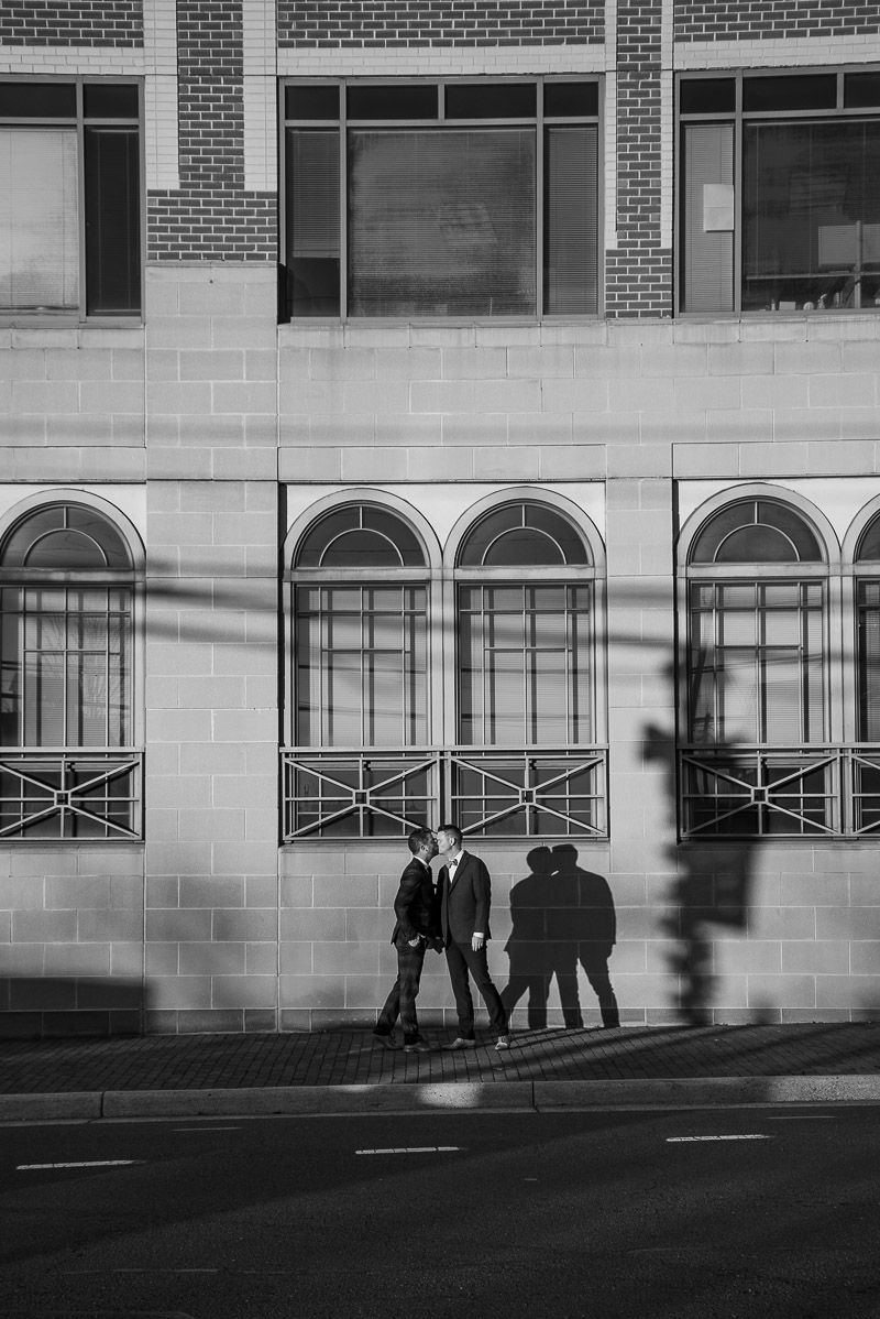 Black and white architectural photograph showing silhouettes of people walking past a brick building with arched windows.