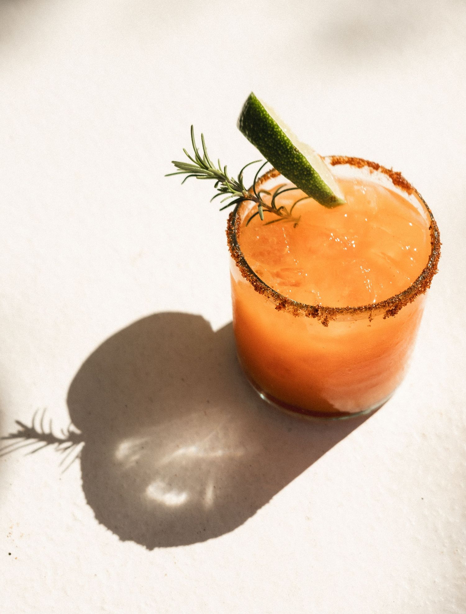 A spicy mezcal margarita with a chili-salt rim, garnished with lime and rosemary, served in a rocks glass.