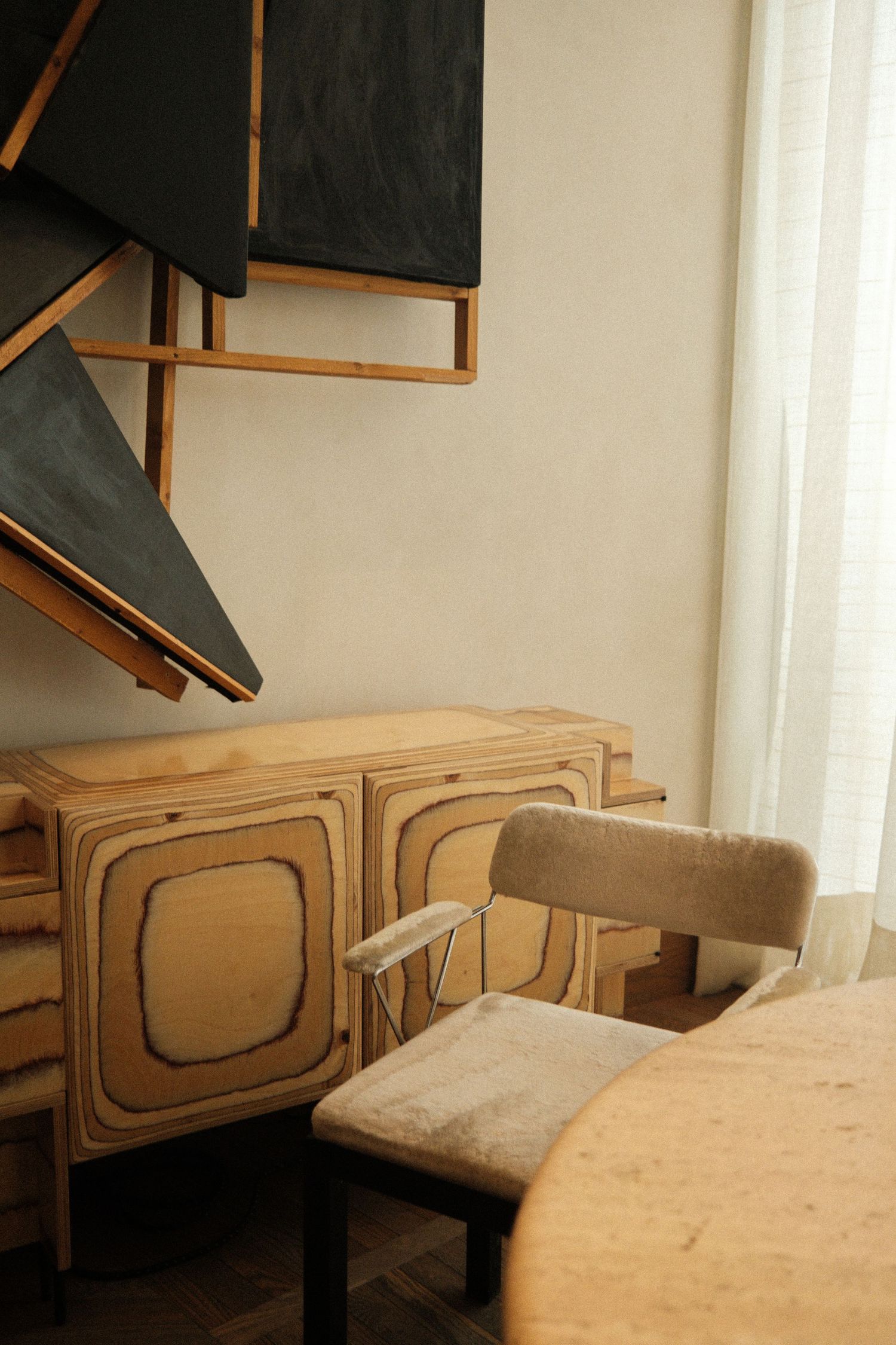 Wooden cabinet or sideboard with geometric panel details and a beige cushioned bench in a minimalist interior setting.