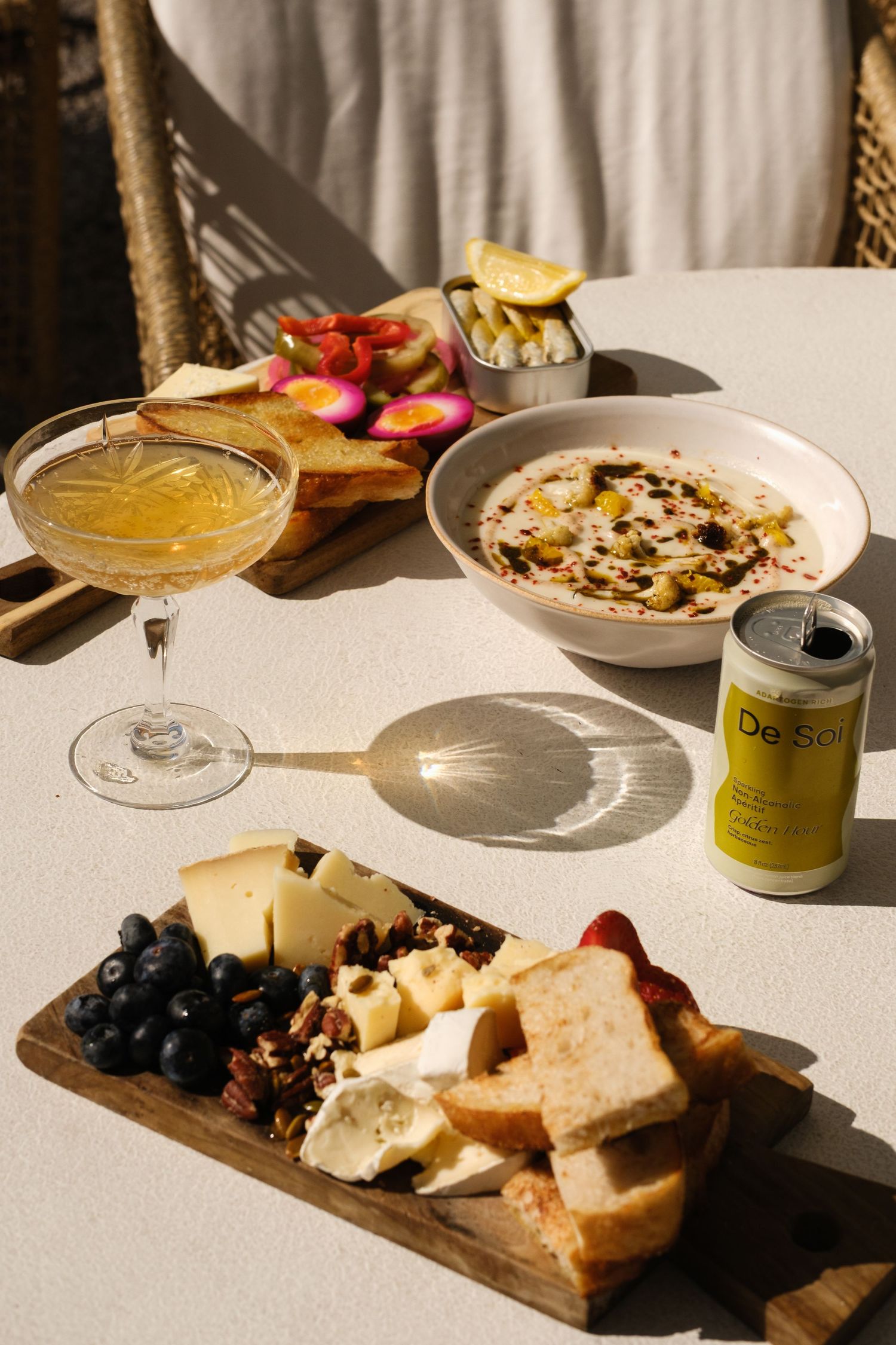 Elegant charcuterie board with cheese, blueberries, bread, and nuts beside a cocktail and De Soi can.