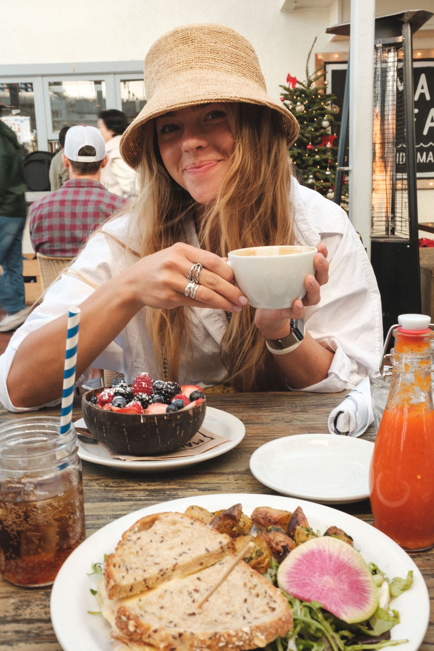 Person in straw hat enjoying brunch with coffee and plates of food at a rustic wooden table.