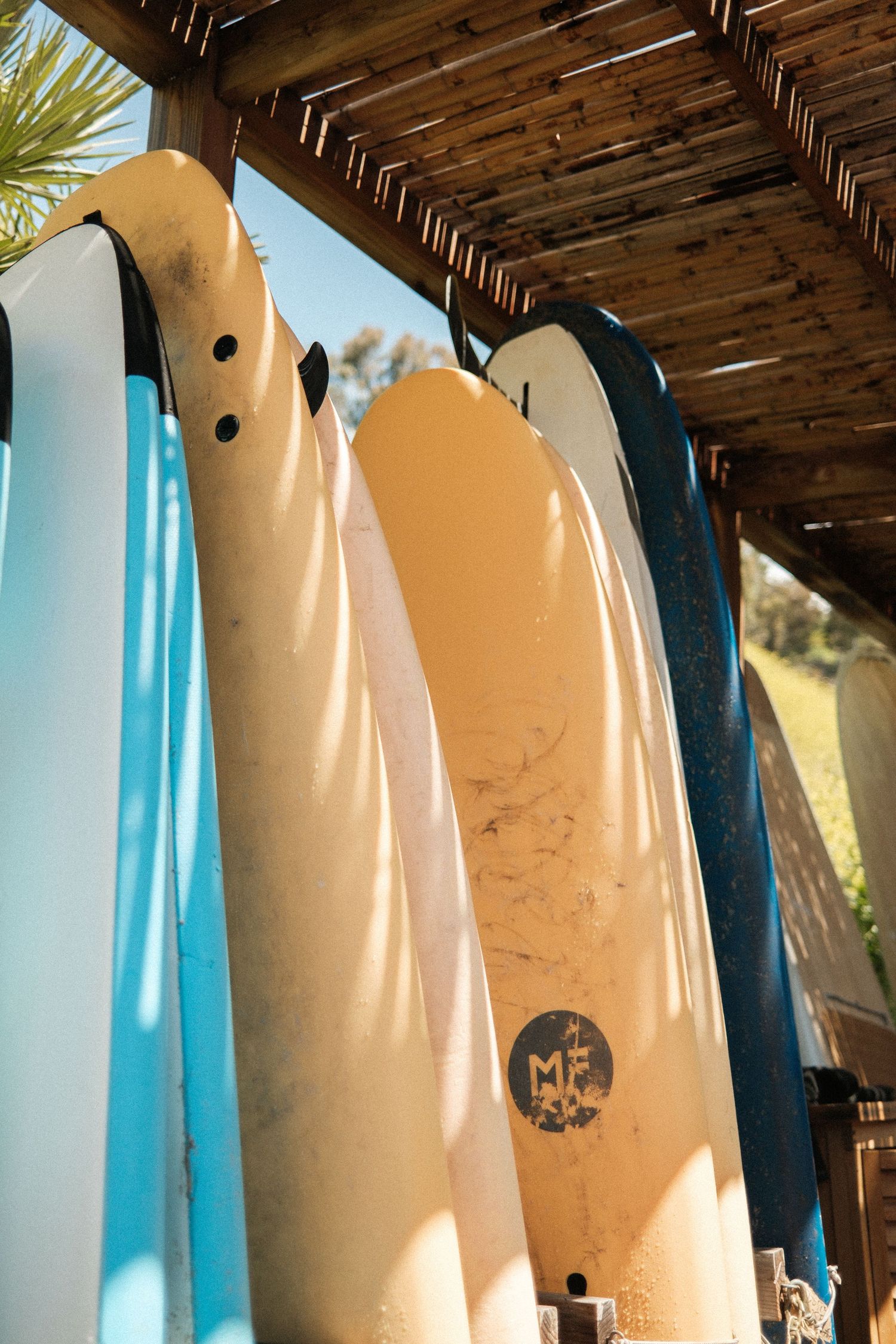 Collection of surfboards displayed under a wooden pergola with natural lighting.