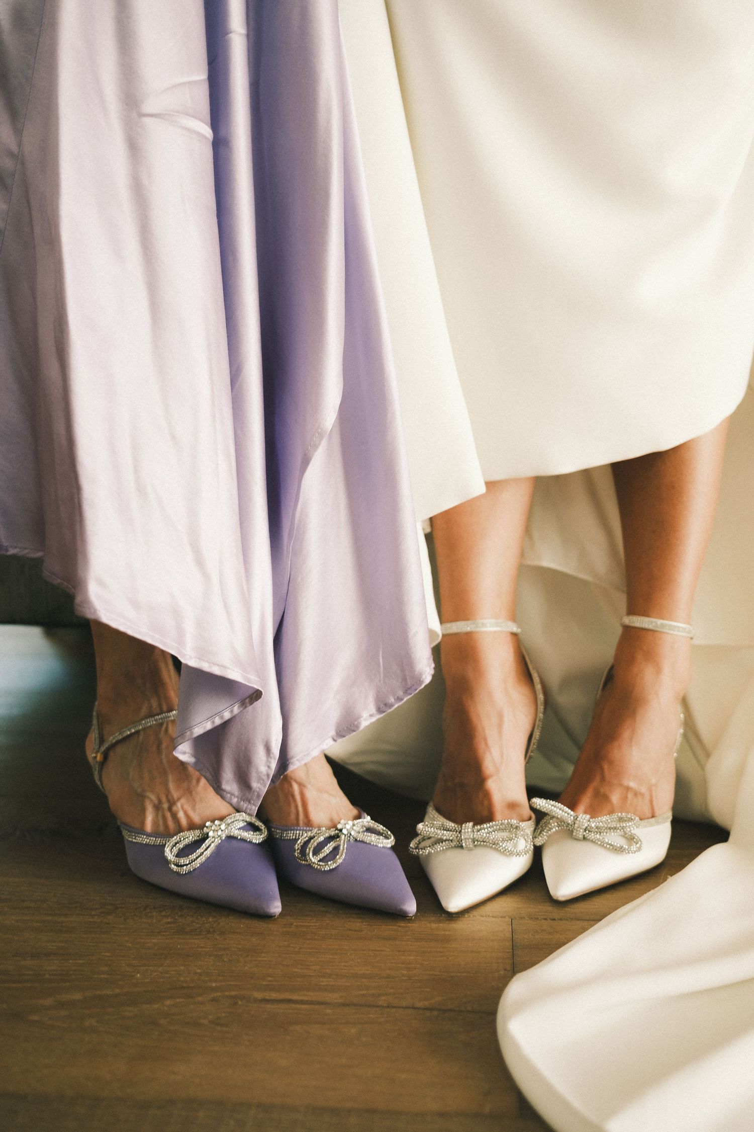 Bride and bridesmaid wearing elegant bow-embellished heels in white and lavender, complementing their formal gowns.