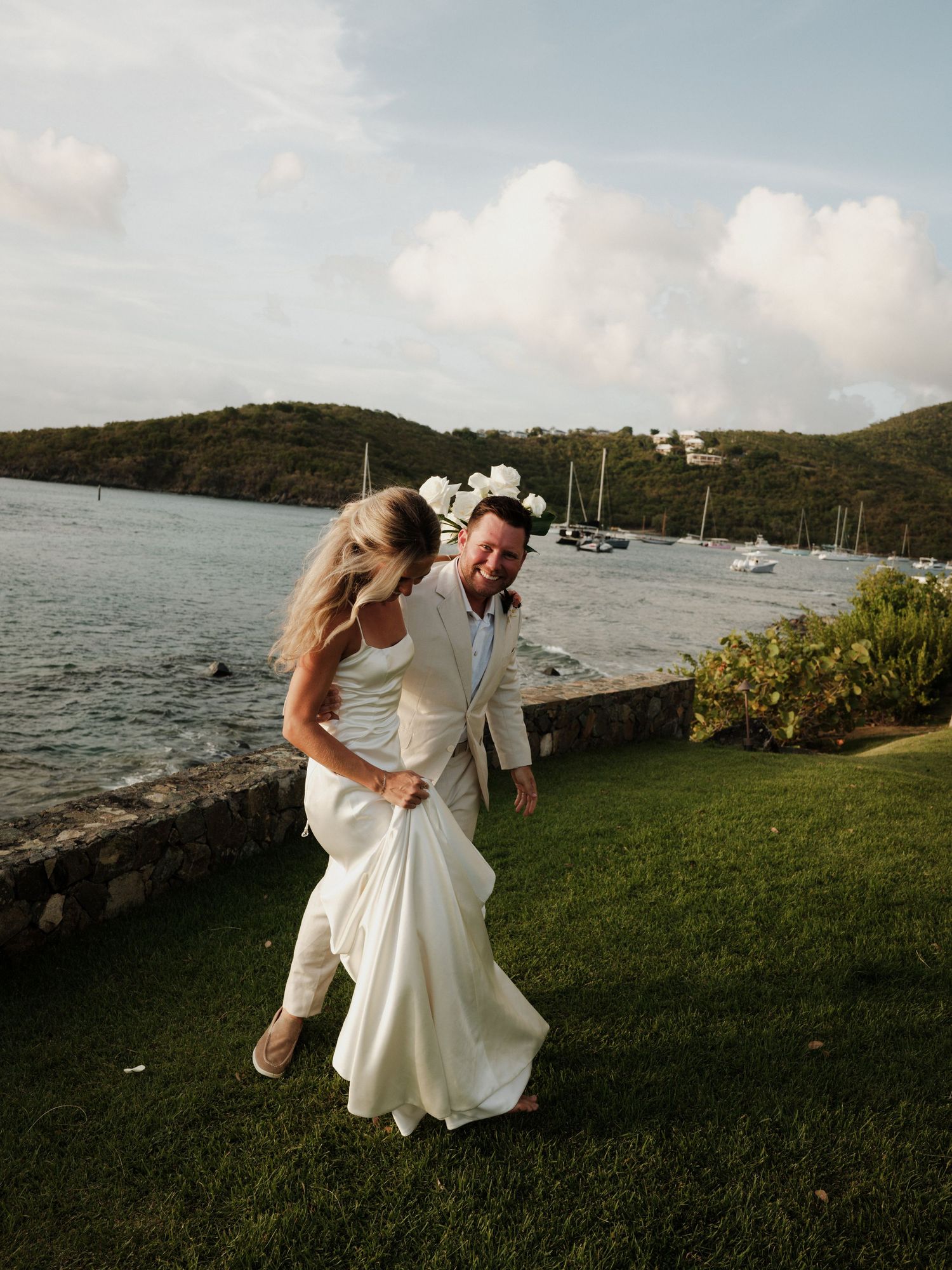 Bride and groom laughing together on waterfront lawn at tropical island wedding venue.