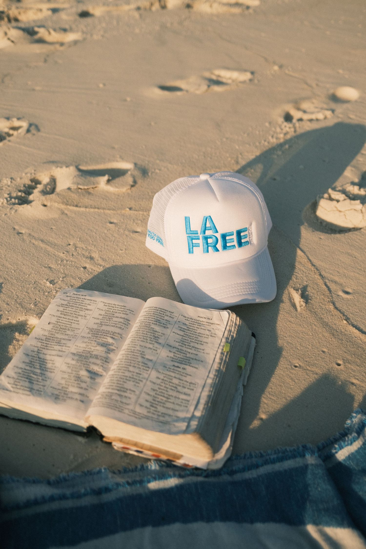 White baseball caps and an open book rest on sandy beach in soft sunlight.