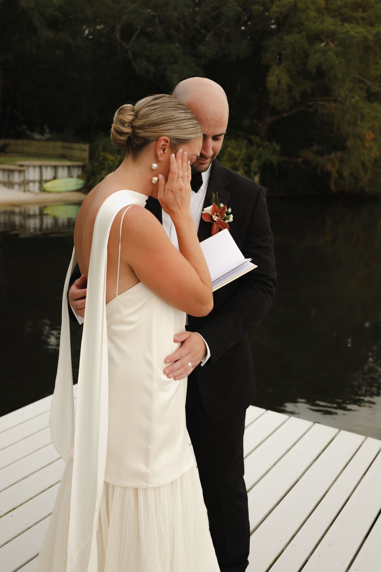 Emotional first look moment between bride and groom standing on a white dock by a serene lake.