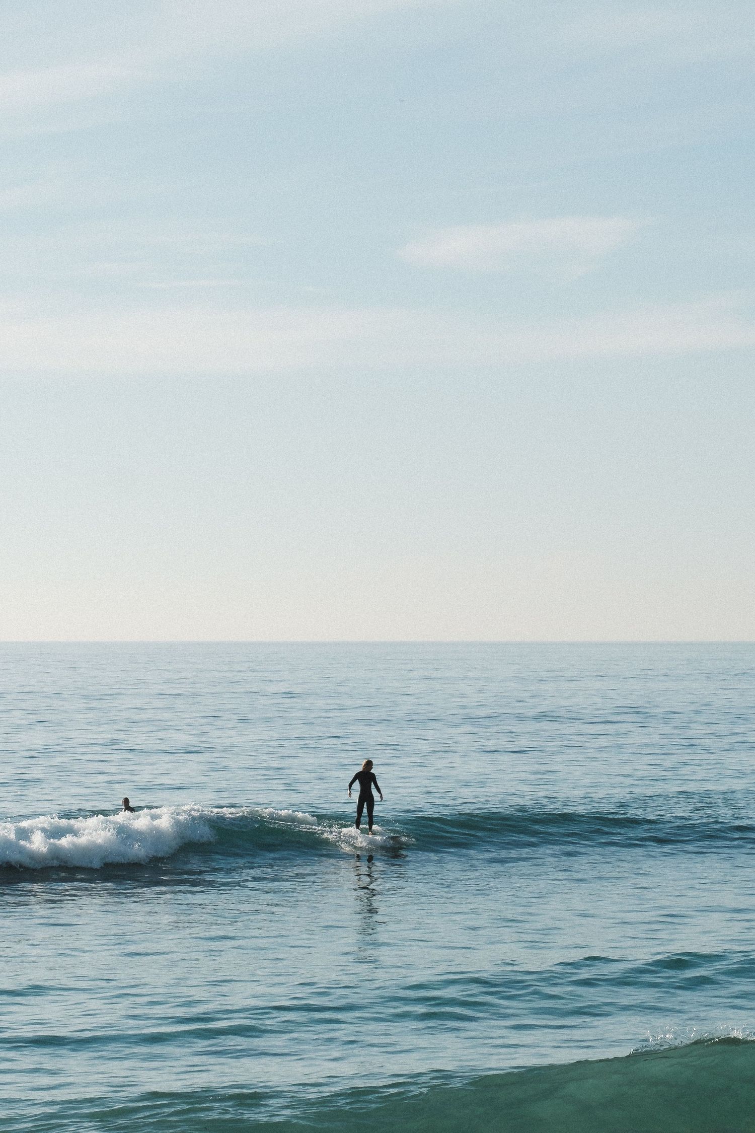 A lone surfer rides a gentle wave in the calm blue ocean on a bright day.