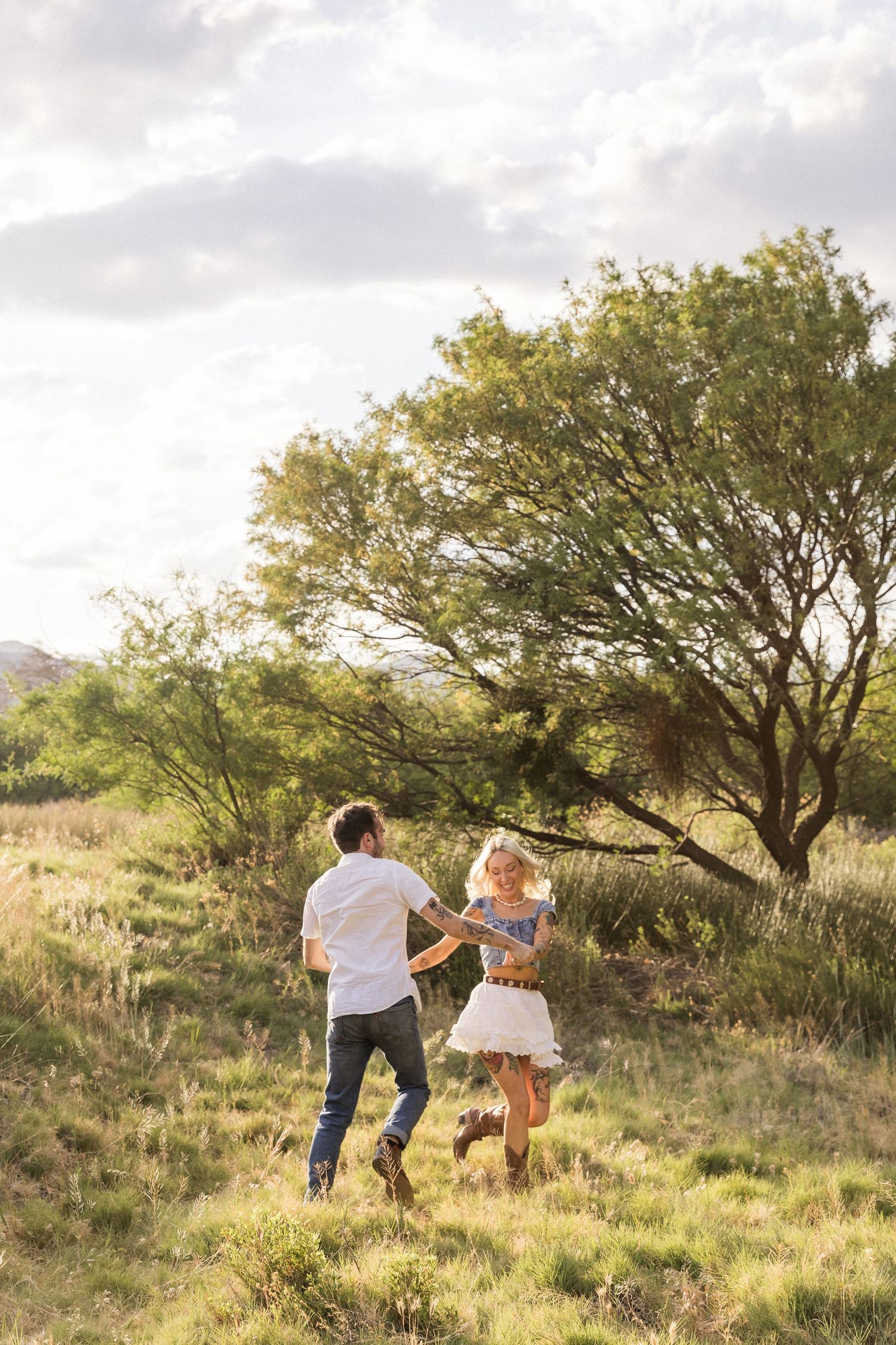 Couple walking through golden grass on a hillside with scattered trees at sunset in North Carolina.