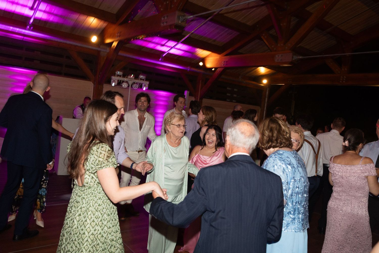 Guests dancing and celebrating at an elegant wedding reception with purple ambient lighting in a rustic venue.