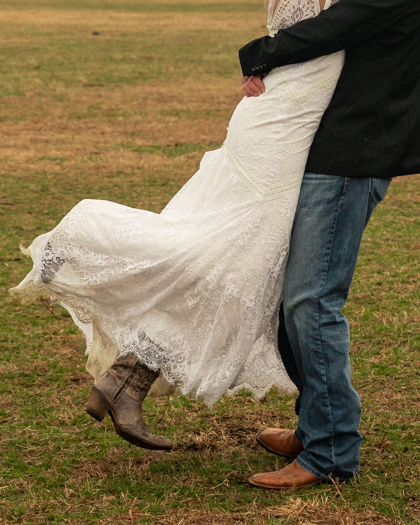 North Carolina Wedding Photographer. Bride in lace wedding gown and cowboy boots dancing with groom in jeans on rustic grass field.