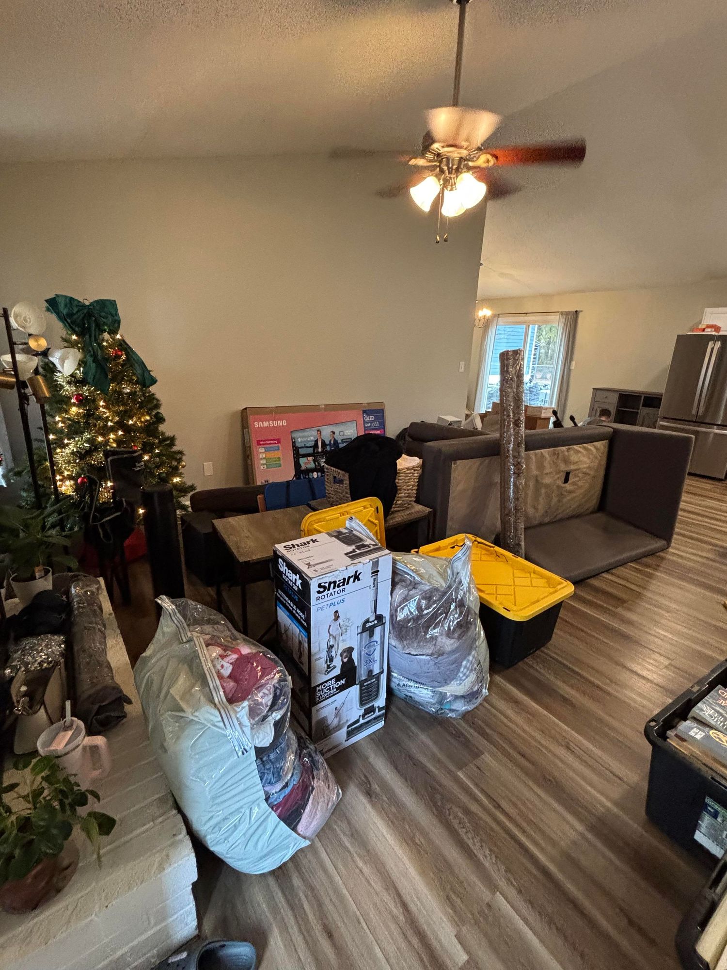 Living room with hardwood floors, ceiling fan, Christmas tree, packed boxes and bags ready for moving.