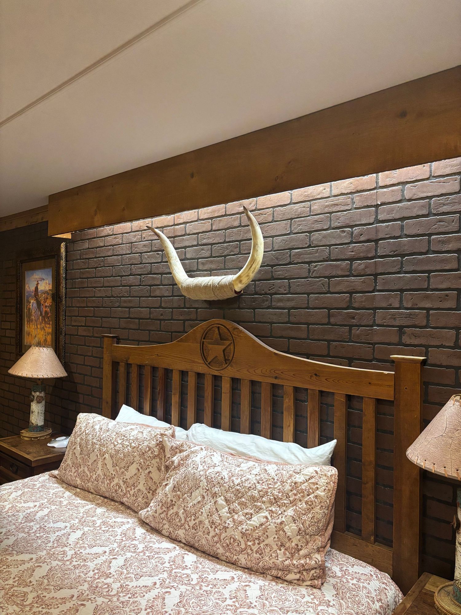 Rustic bedroom with wooden star headboard, longhorn mount on brick wall, and matching bedside lamps.