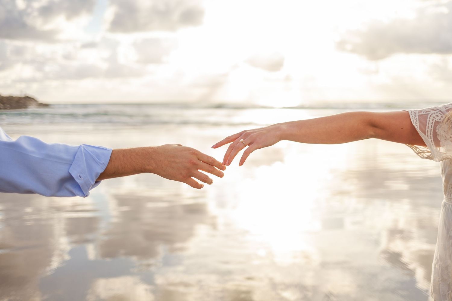 Two hands reach towards each other at Wilmington North Carolina Beach, sunset sky and clouds in the background creating a silhouette effect.