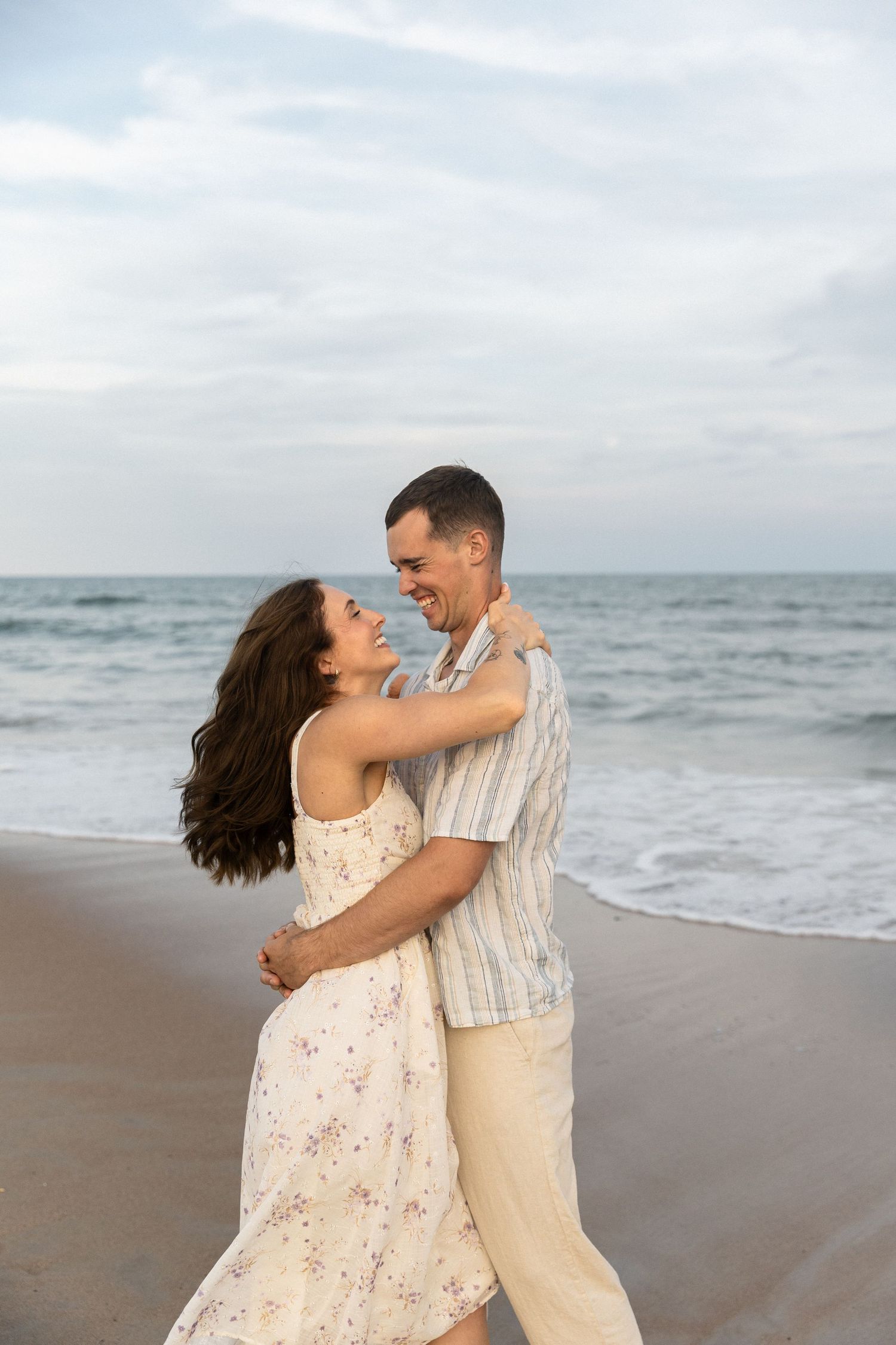 couple laughing on the beach as the sun slowly dips behind the horizon