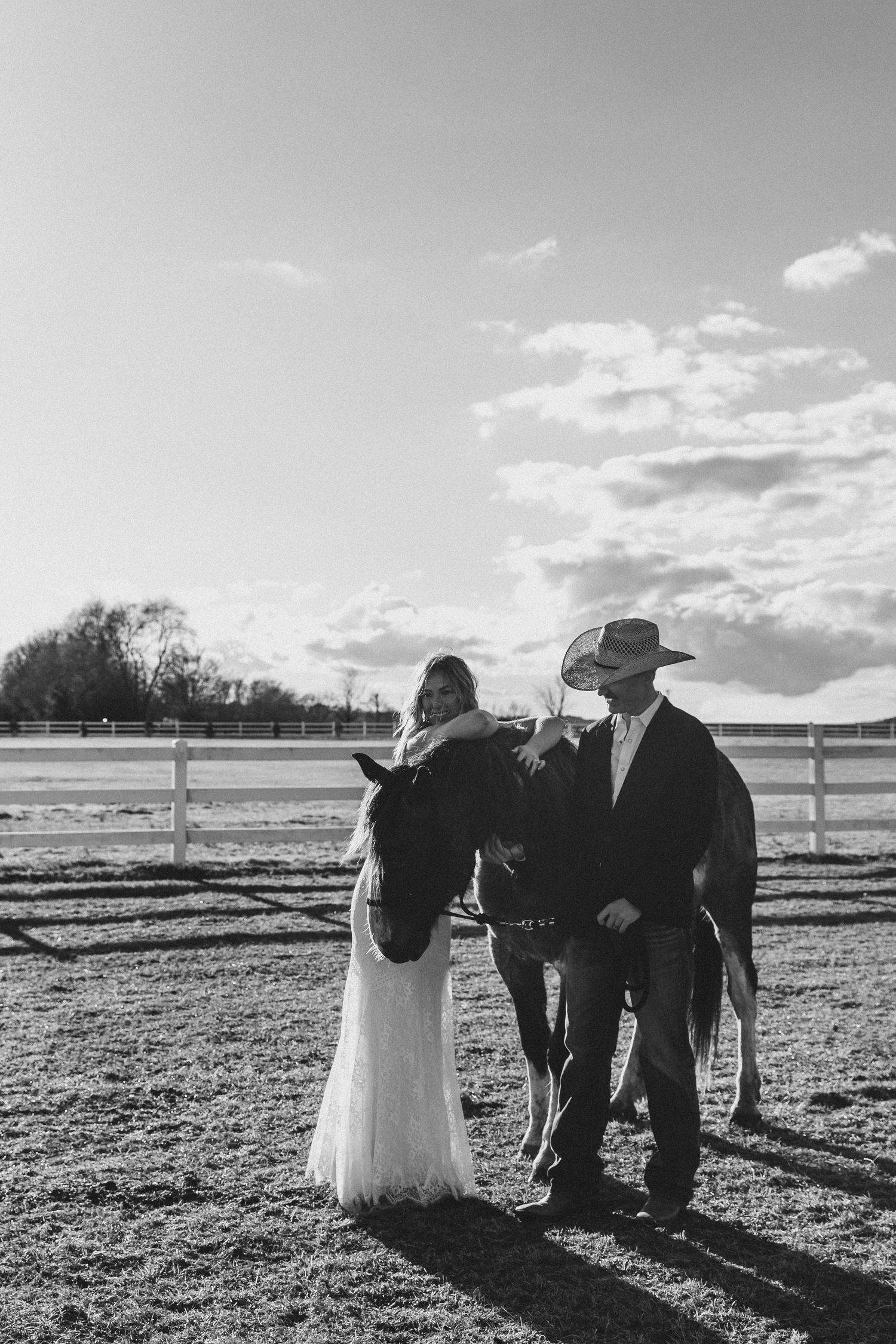 Black and white photo of a bride and groom standing with a horse at a rustic ranch wedding venue in North Carolina.