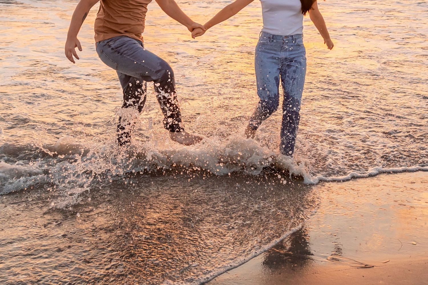 Couple holding hands and splashing in ocean waves at sunset on a beach in Crystal Coast North Carolina